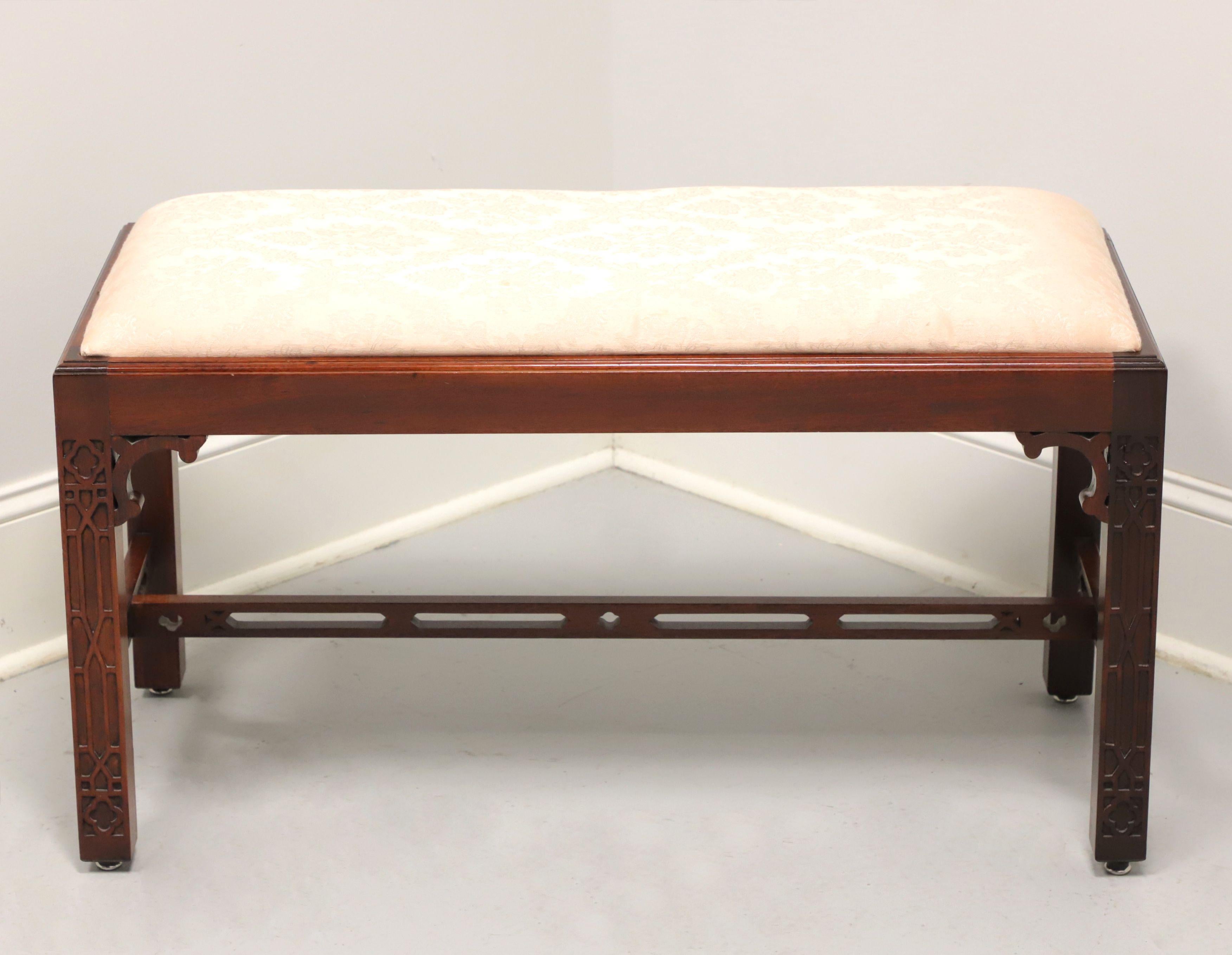 A Chippendale style bench by Baker Furniture, from their Cliveden Place Collection. Solid mahogany, upholstered seat, carved corner pieces, decorative fretwork details to the straight legs, and open carved stretchers. Features a pink color brocade