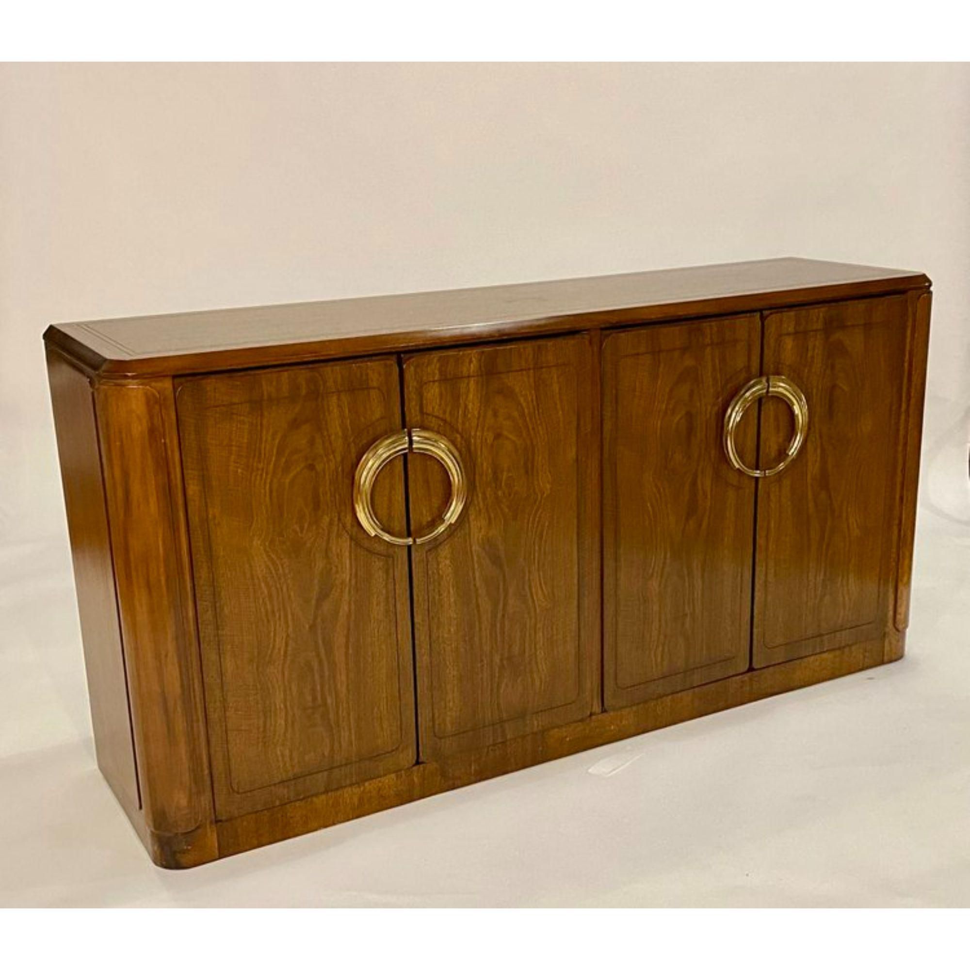 Stunning early 1980's Art Deco Revival design buffet by Baker. This credenza is well crafted from solid walnut with lovely details that wrap around the sides as well as ornamented brass handles which echo the designs of an Art Deco era. The