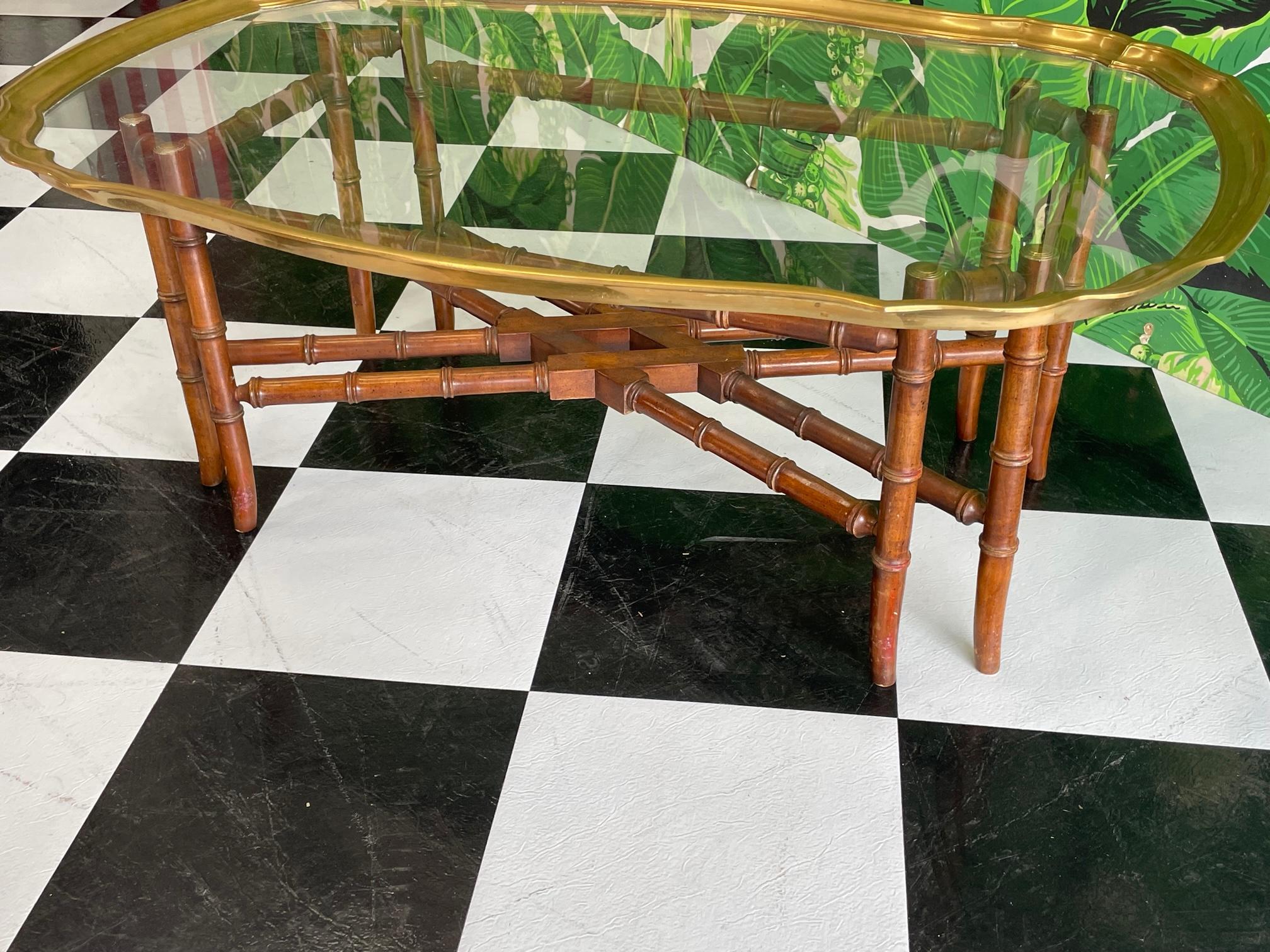 Regency style faux bamboo coffee or cocktail table attributed to Baker features a glass top cut to fit a decorative brass frame. Brass capped legs supporting the top. Good condition with minor imperfections consistent with age, see photos for