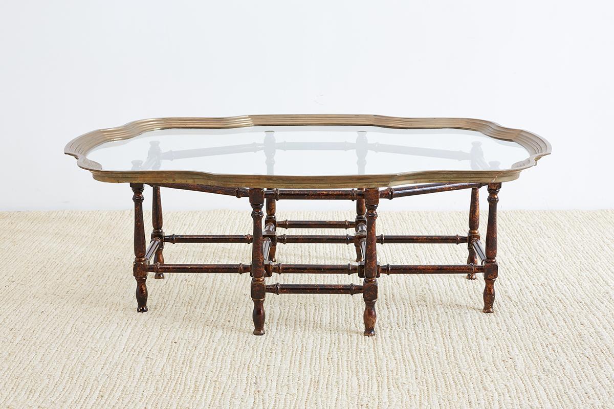 Hollywood Regency style Baker coffee table featuring an octagonal base with a faux bamboo look. Finished in a tortoise shell lacquer over a gilt base. Topped with a large brass tray top with an interesting scalloped edge and a stepped border.