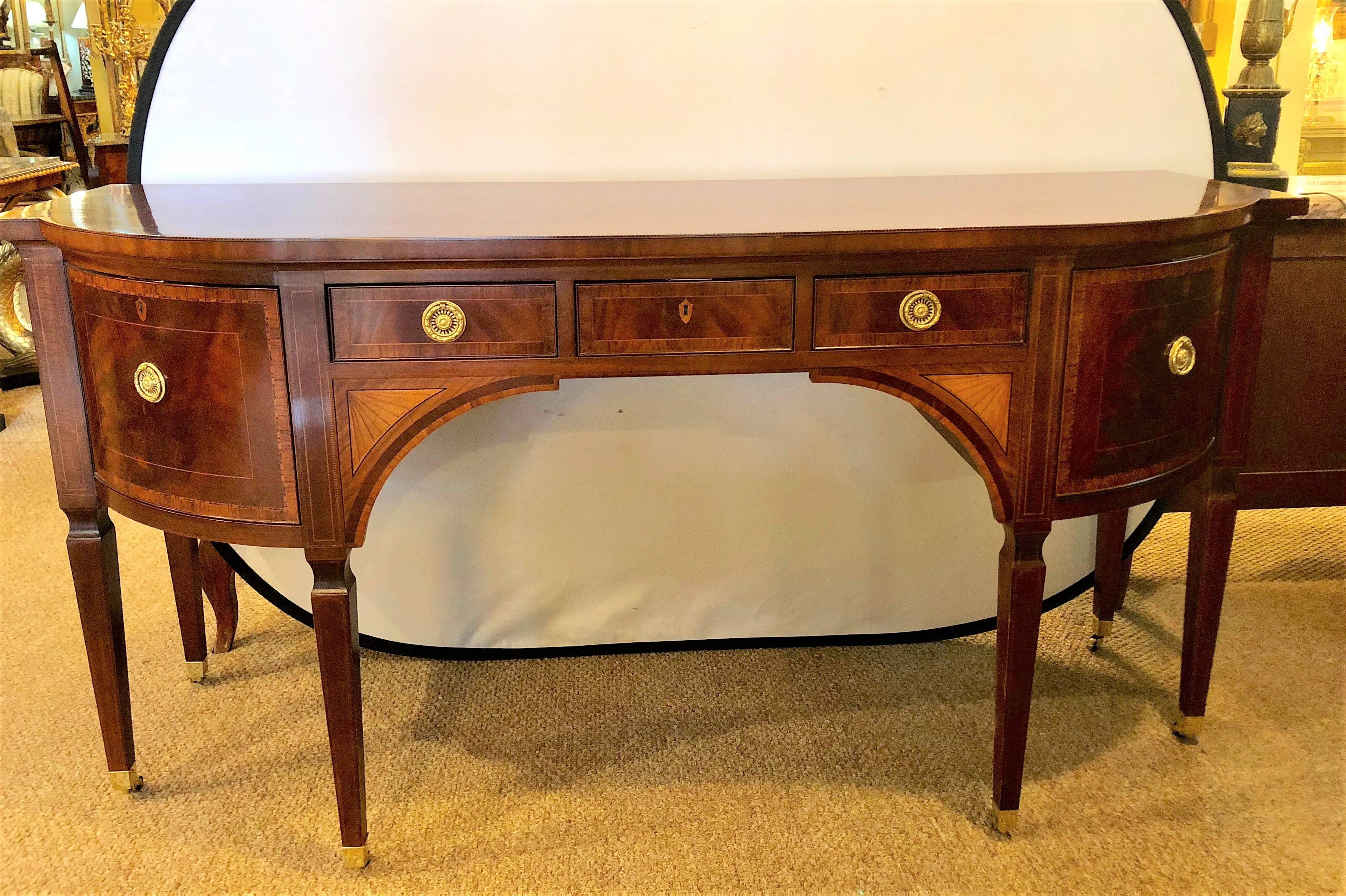 A Baker Federal style fine satinwood inlaid sideboard. This wonderful Baker Furniture Company sideboard or server sits on brass casters leading to fine tapering legs which support an upper case having a center group of three drawers flanked by