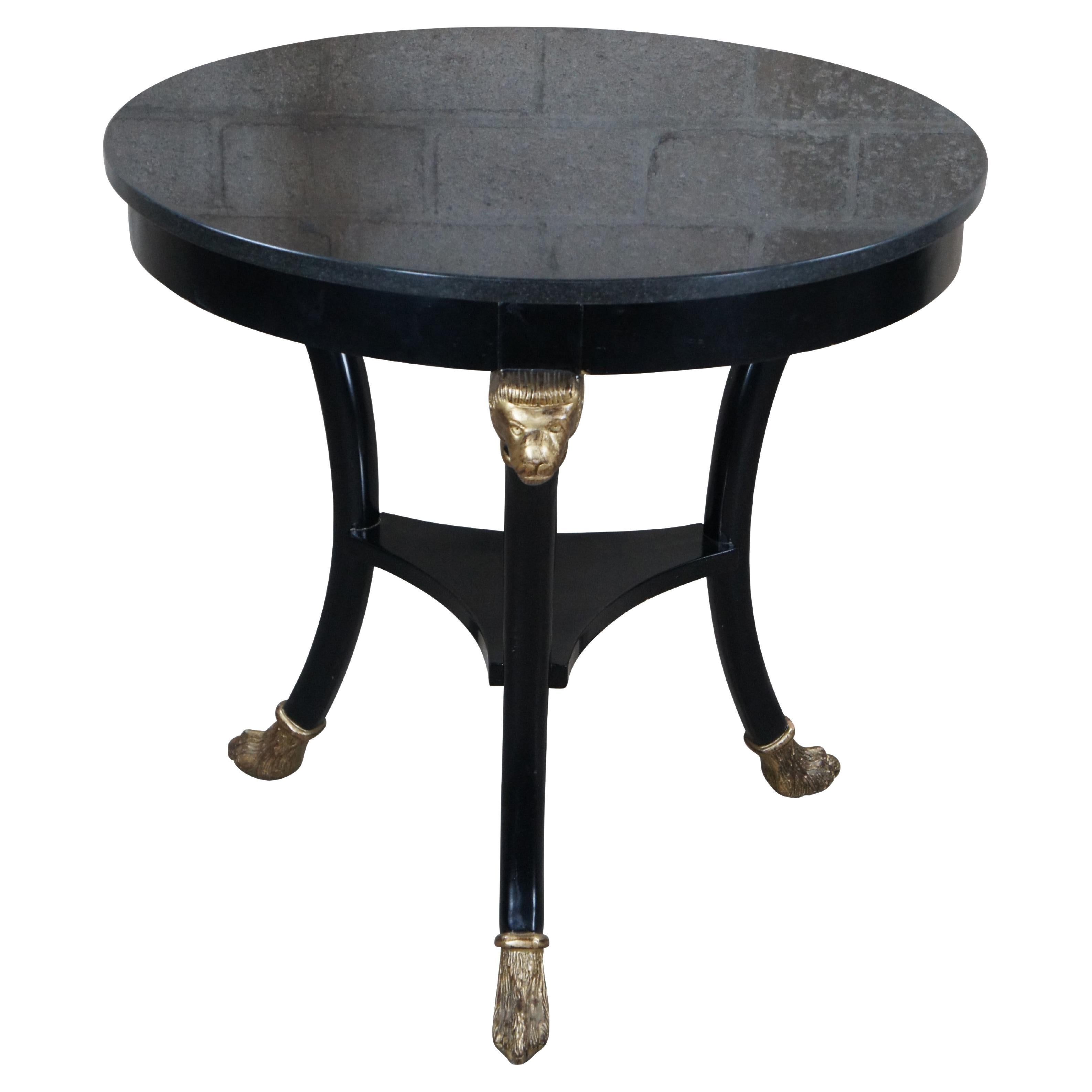 Tavolino Gueridon di ispirazione Empire / Regency / Neoclassica della fine del XX secolo. Presenta una struttura in legno duro ebanizzato con piano in granito scuro. La forma rotonda è sostenuta da tre gambe sagomate con teste di leone rifinite in