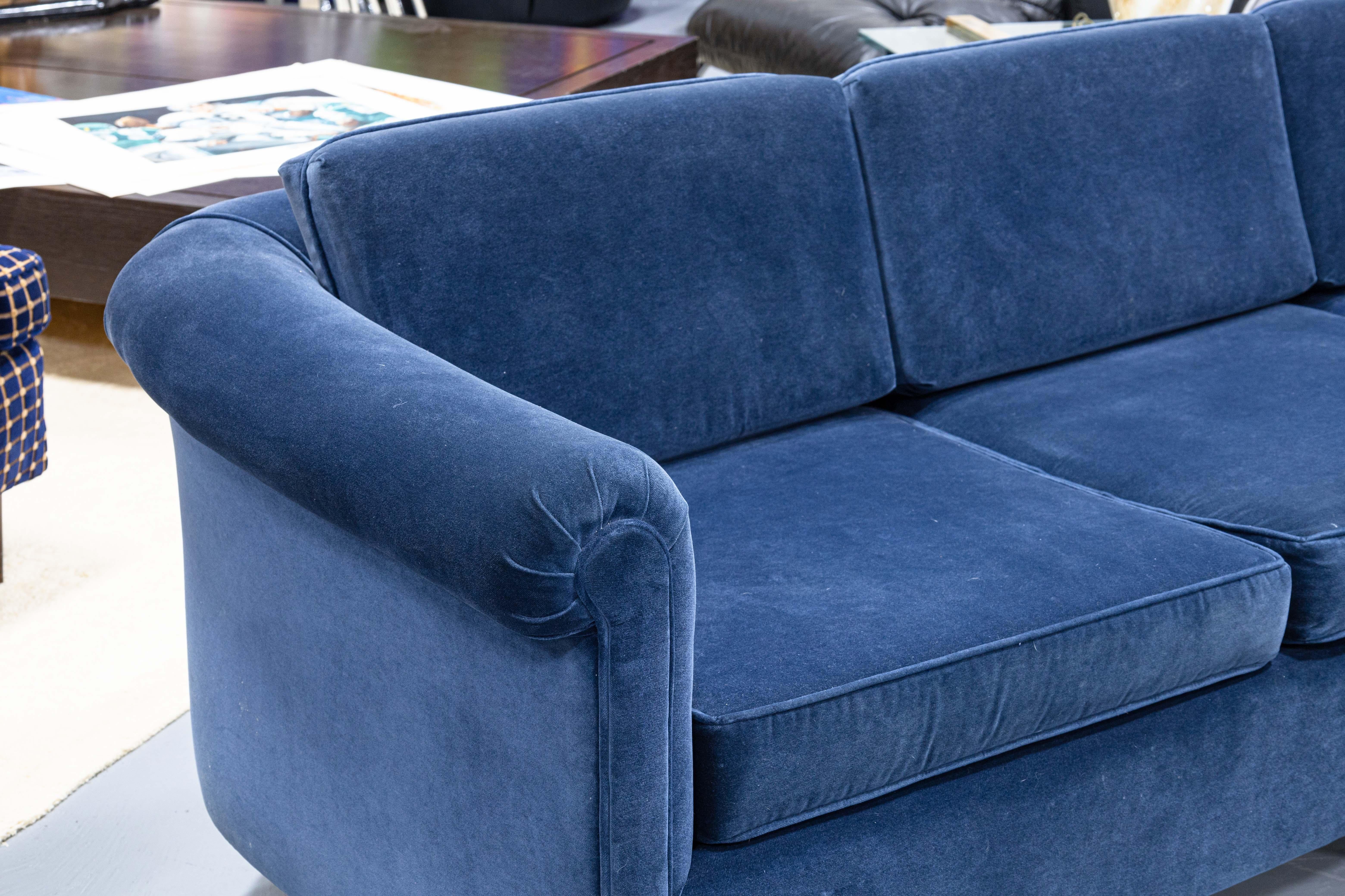 A Baker Furniture velvet sofa. This beautiful piece of contemporary modern furniture features a classic styling, with a bucket frame, roll arms, and tapered wooden legs rounding the base of the sofa. This piece is upholstered in a gorgeous deep,