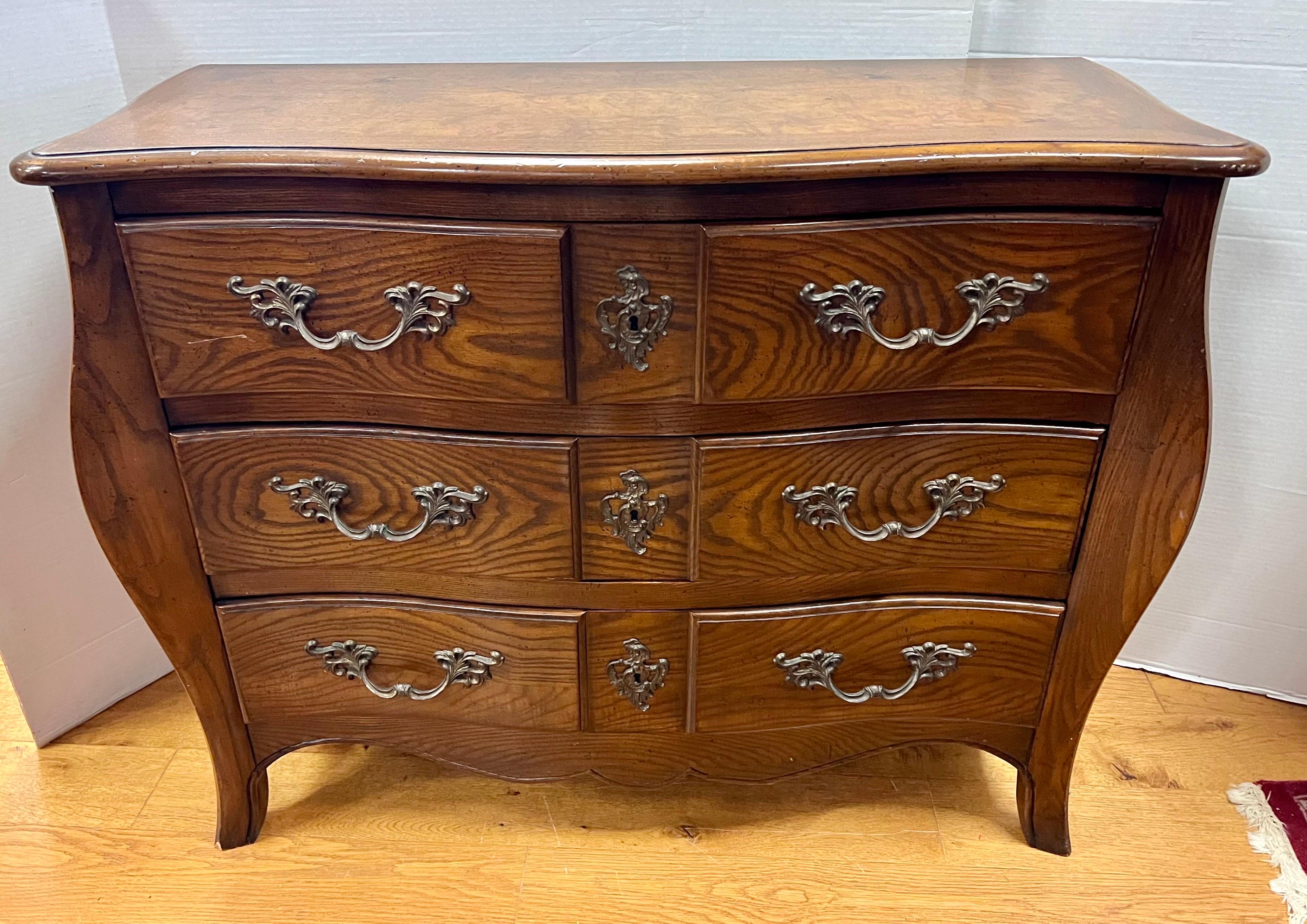 Elegant and coveted bombe chest commode by Baker Furniture Company.
Features three dovetailed drawers with ornate, original hardware.  Baker medallion present inside drawer as shown.