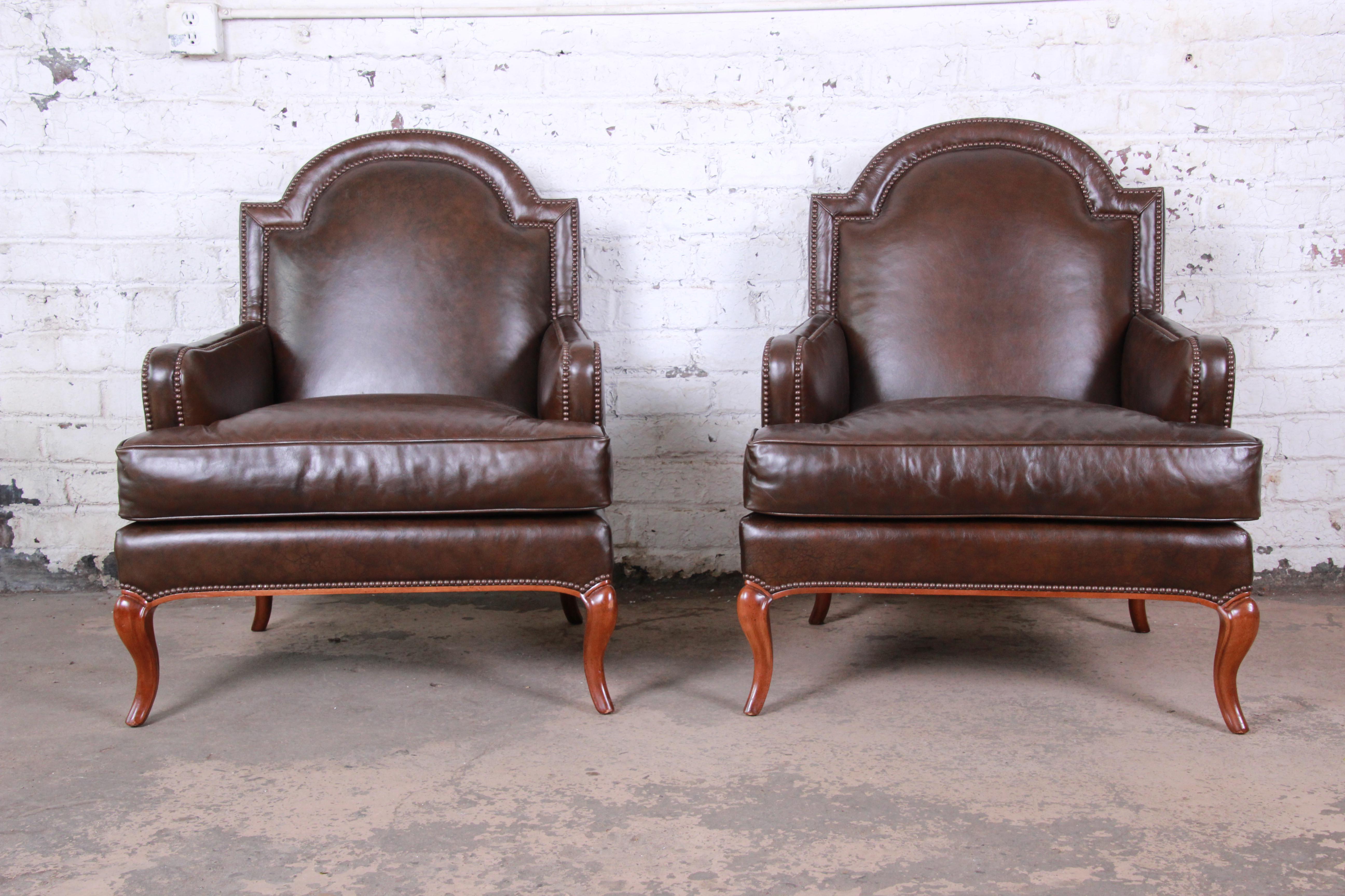 An exceptional pair of leather lounge or club chairs by Baker Furniture. The chairs feature gorgeous high-end studded brown leather, with cabriole legs. They have a nice patina and are extremely comfortable. The original Baker label is present on