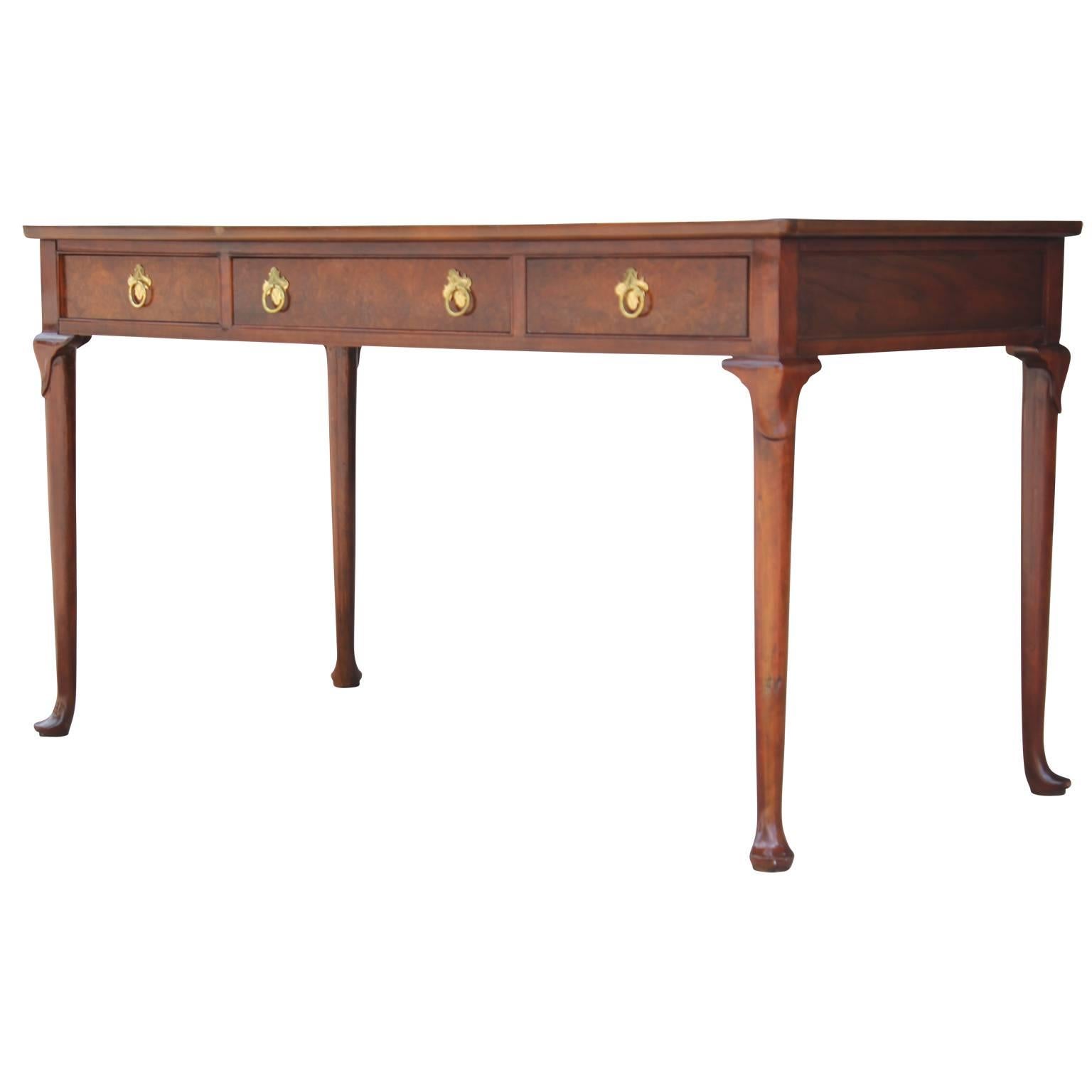 Lovely burl and walnut Queen Anne writing table or desk made by Baker Furniture. This piece is in very nice, vintage condition and can be used as either a writing table, or a desk. This desk is has three drawers, accompanied with four marvelous