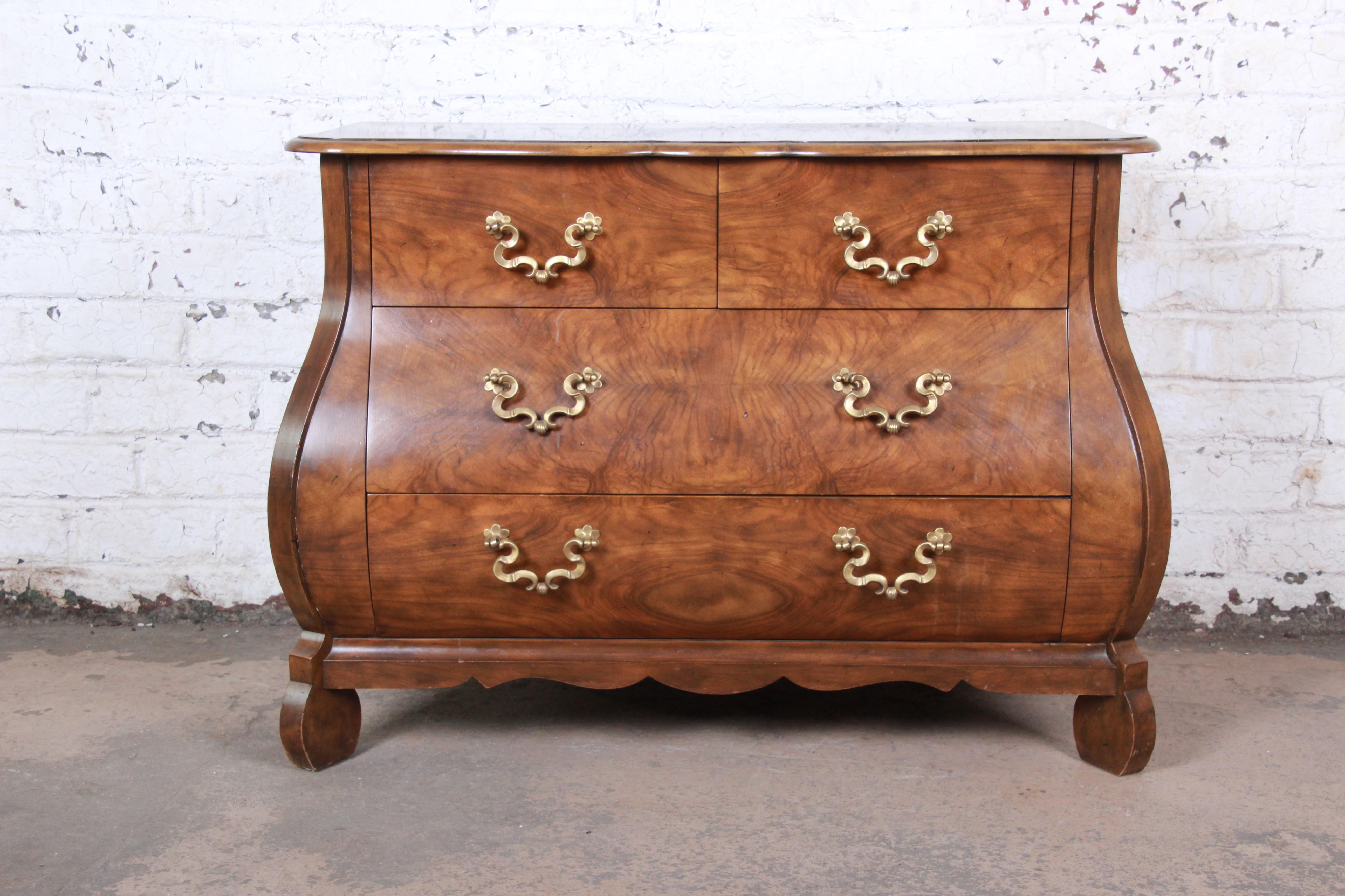 An exceptional French style Bombay chest or commode by Baker Furniture. The chest features gorgeous burled walnut wood grain, with a scalloped top and apron and canted corner front legs. It offers good storage, with four deep dovetailed drawers,
