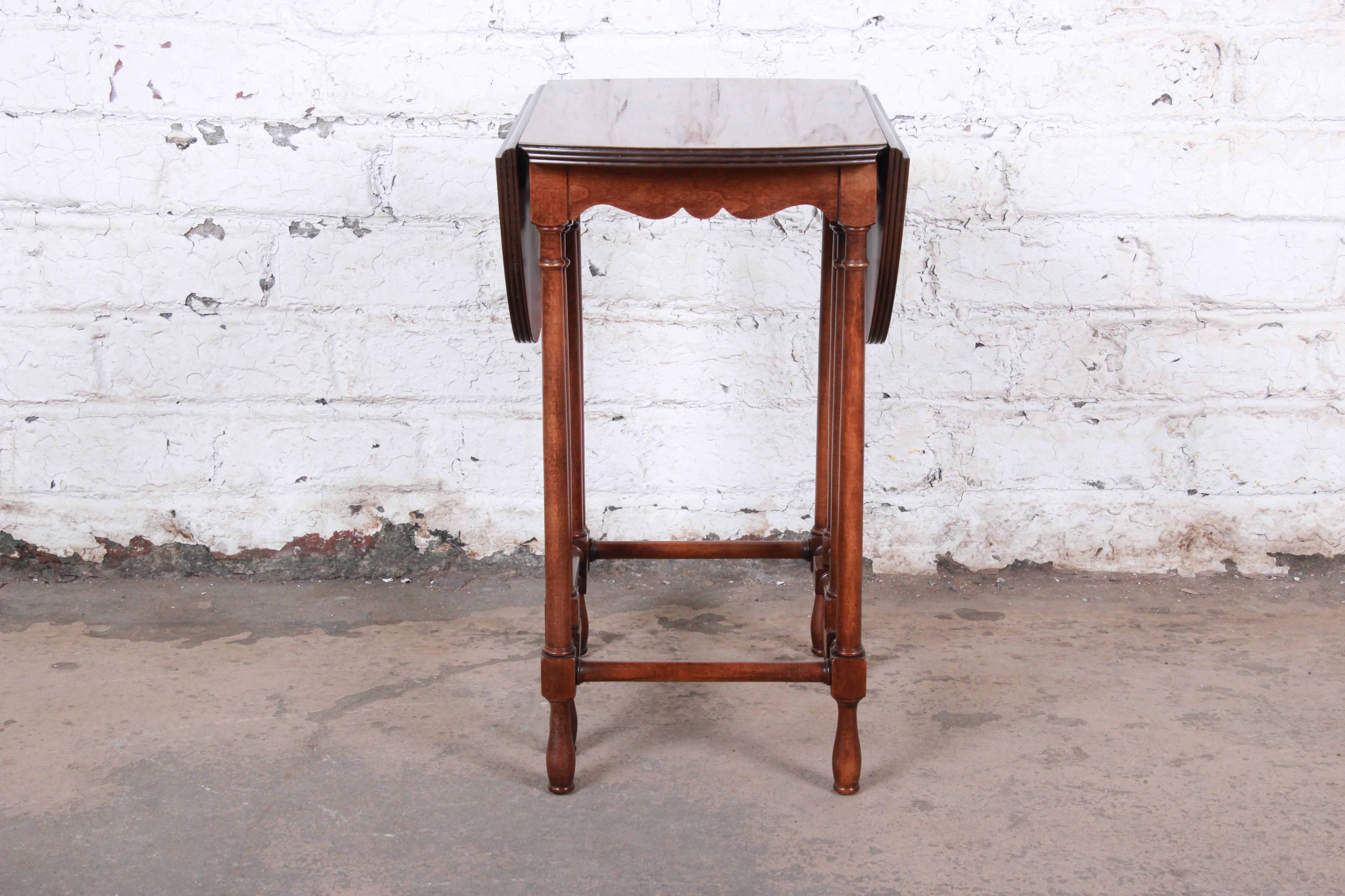 A beautiful gate leg drop leaf side table by Baker Furniture. The table features a gorgeous burled walnut top and solid walnut legs. The original Baker label is present on the underside. The table is in excellent original vintage