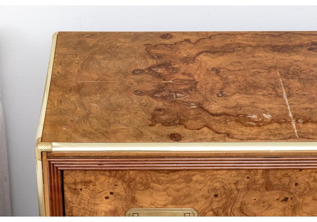 Baker Furniture campaign style three drawer chest with brass trim around the top and vertically flanking the drawers. The three drawers are framed with reeded wood trim and accentuated with embossed brass corners and inset brass hardware. The chest