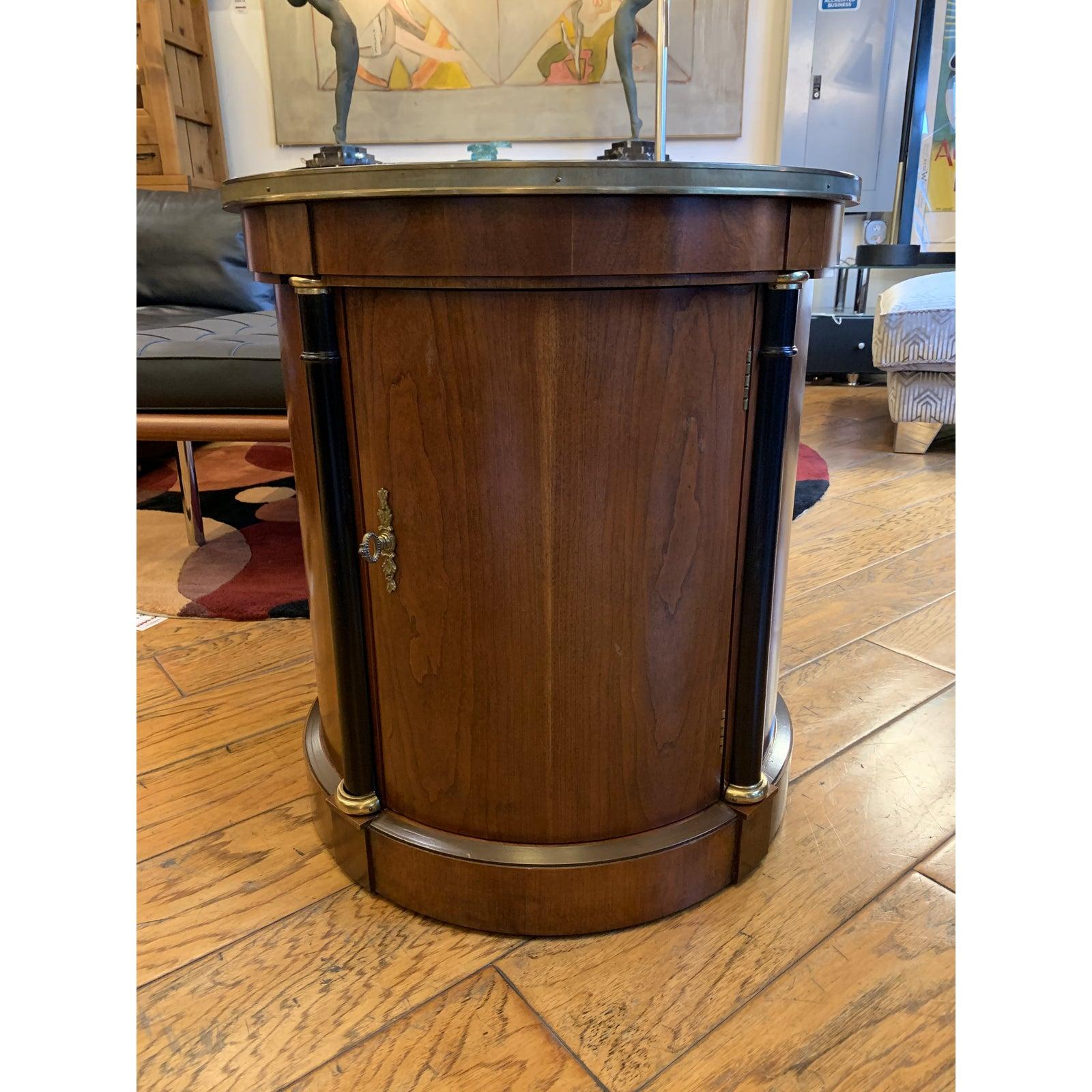 A Baker Furniture cherry Model #4359 drum side table. Starburst patterned inlay veneer is beautifully contained within circular drum form. Brass key and lock pull reveals open storage containing optional shelf. Top perimeter is banded in brushed