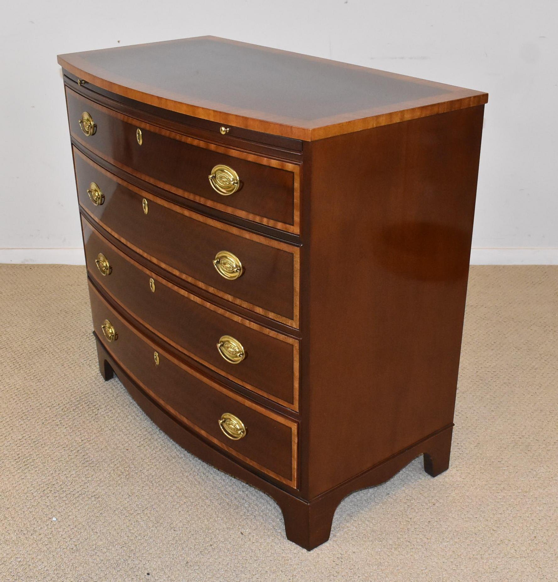 Baker Furniture banded inlay mahogany bow front chest. Satinwood drawer fronts have oval brass hardware. Pull out writing surface. Oak drawer construction.