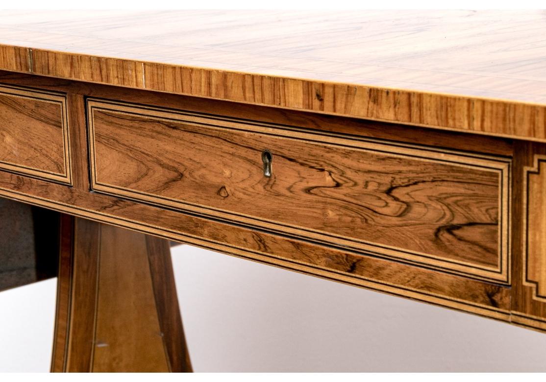 An exceptional Baker Furniture Collector's Edition drop leaf sofa or writing table in an elegant Regency design, finely crafted in dramatically figured yew wood. The tabletop and leaves with cross-banding and ebonized string inlay. With two frieze