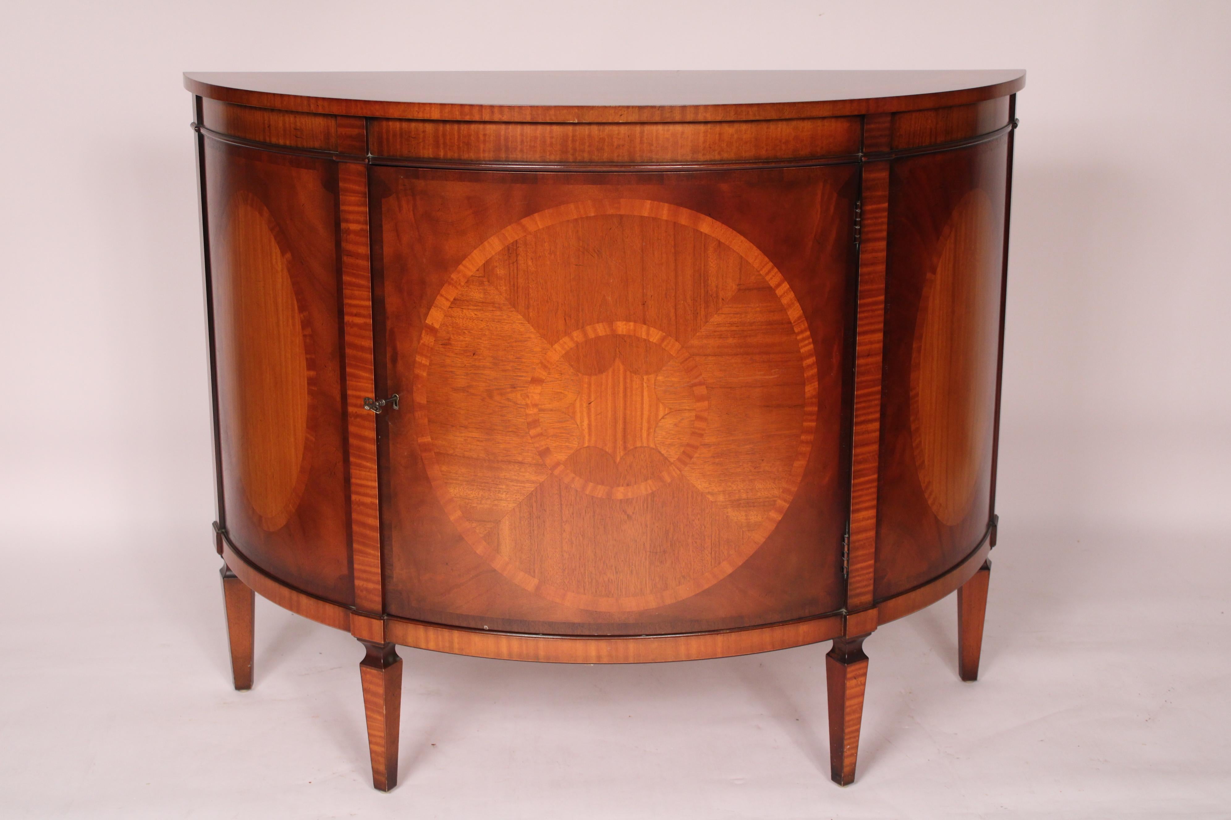 George III style mahogany demi lune cabinet, from Baker Furniture Company's Charleston Collection, late 20th century. With a demi lune shaped top with 3 strands of crossbanding, the sides with oval inlaid panels, a circular inlaid door, resting on