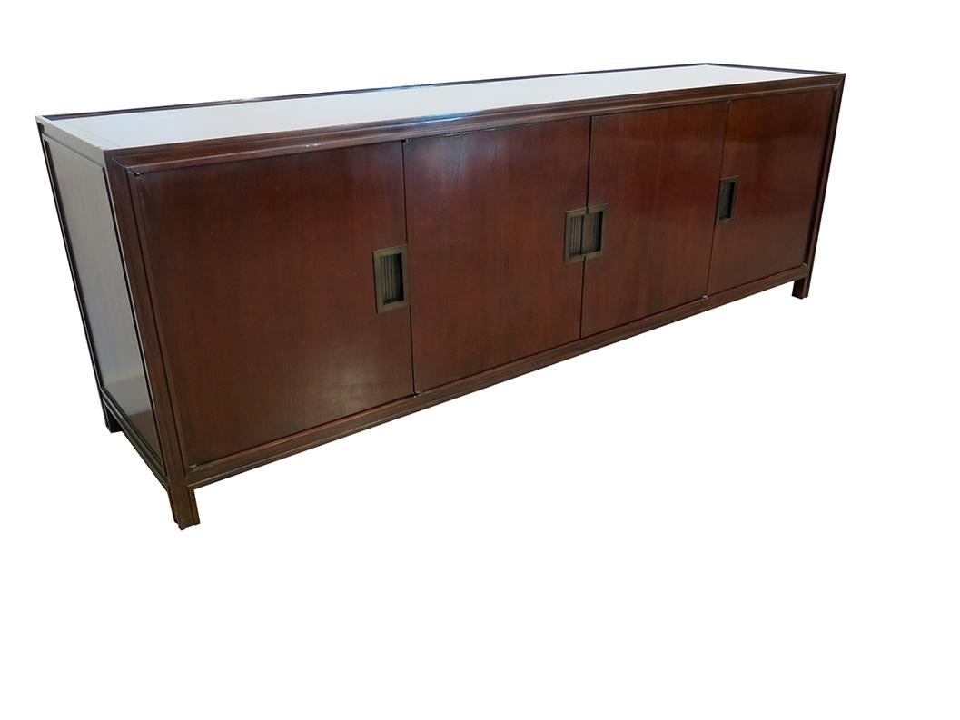 This Baker Furniture Company sideboard is in lacquered mahogany. It has a rich deep brown color with brass hardware. The two center doors open to reveal a large 38.5 inch adjustable and removable shelf. The shelf position can either be 7.5