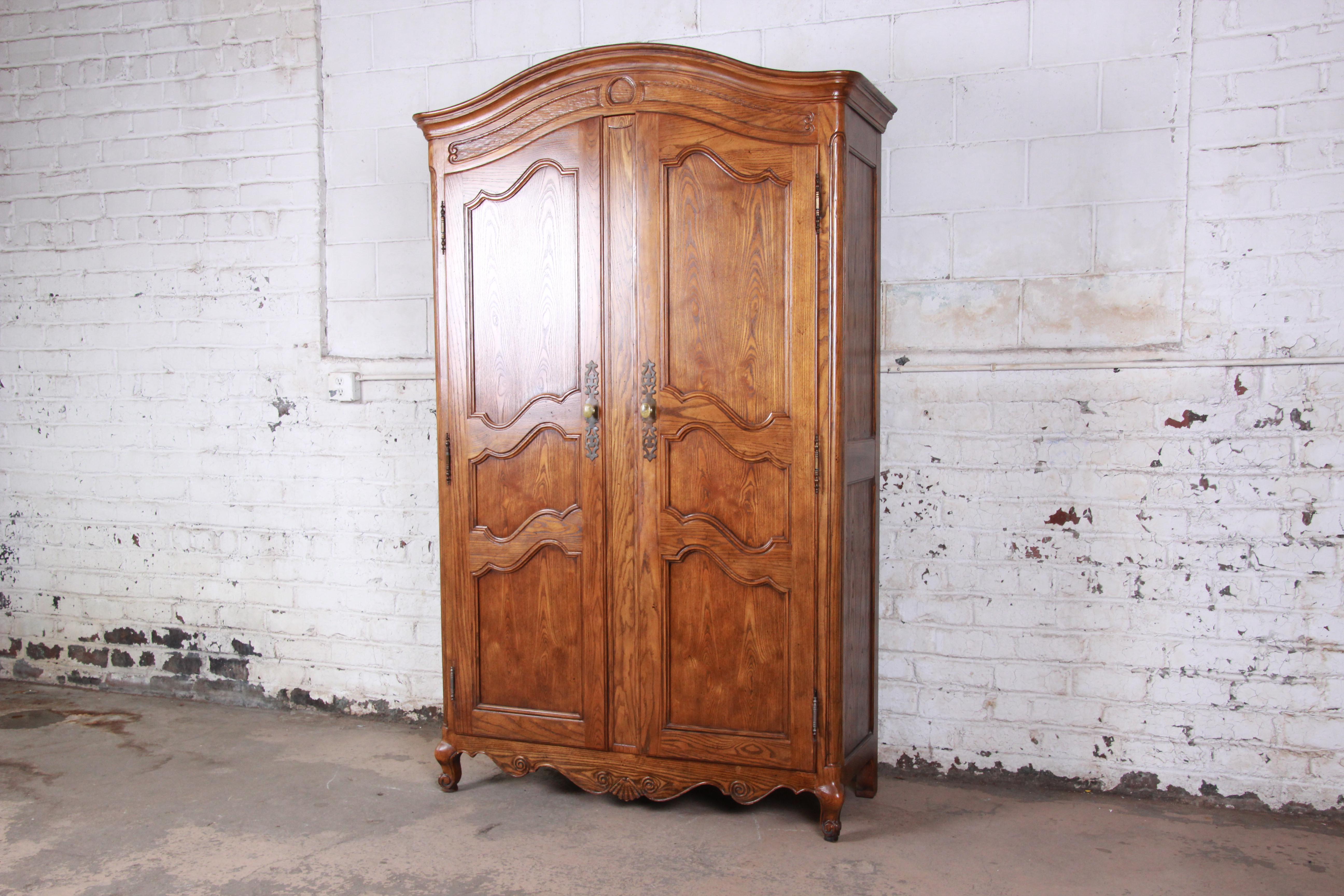 Offering a gorgeous French provincial Louis XV style armoire or wardrobe by Baker furniture. The armoire features beautiful carved wood details and solid oak construction. It offers ample room for storage, with three open shelves, three cubbies, and