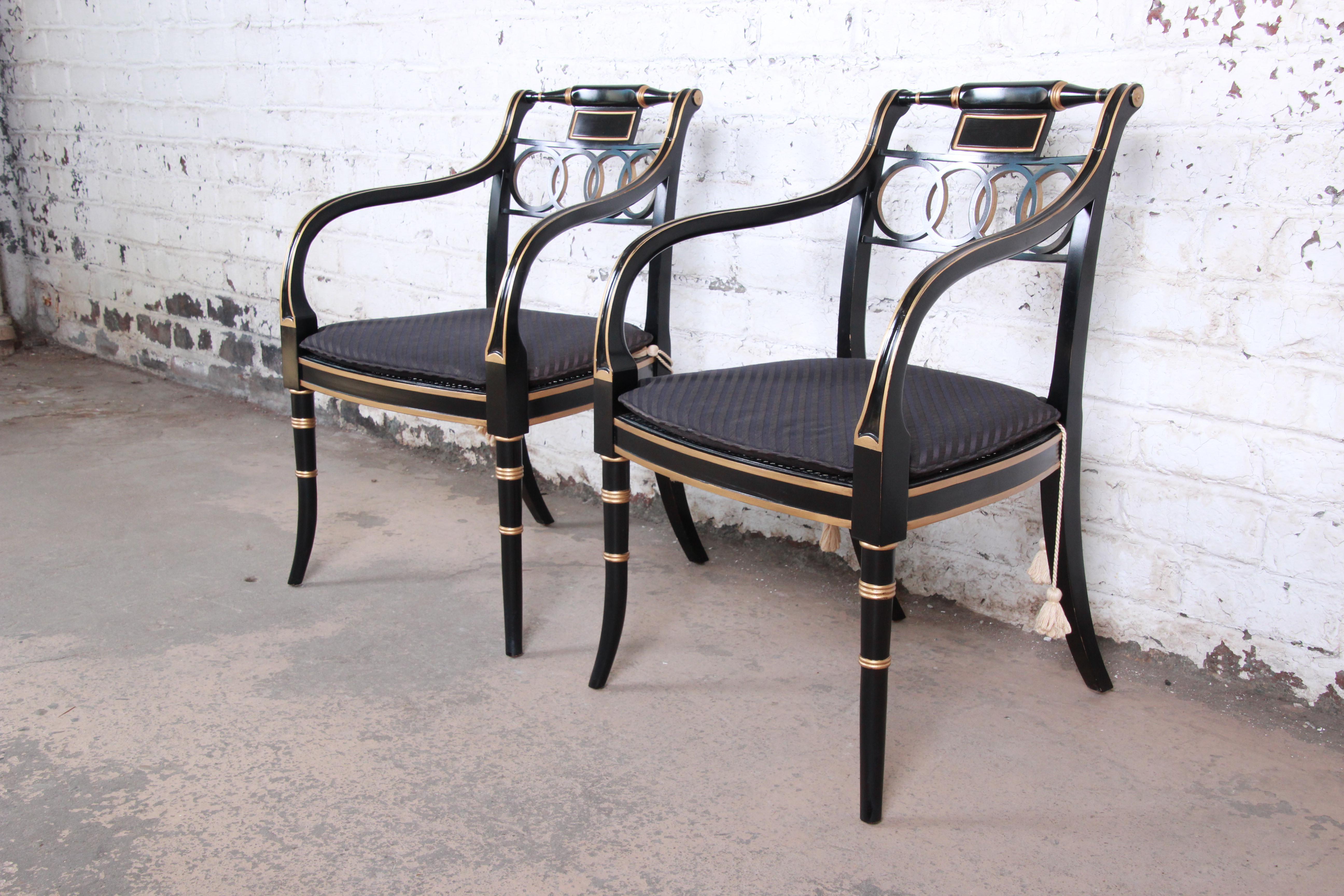 An exceptional pair of Regency style armchairs from the Historic Charleston collection by Baker Furniture. The chairs feature stunning ebonized and gold gilt solid wood frames with caned seats and removable seat cushions. Made with the highest