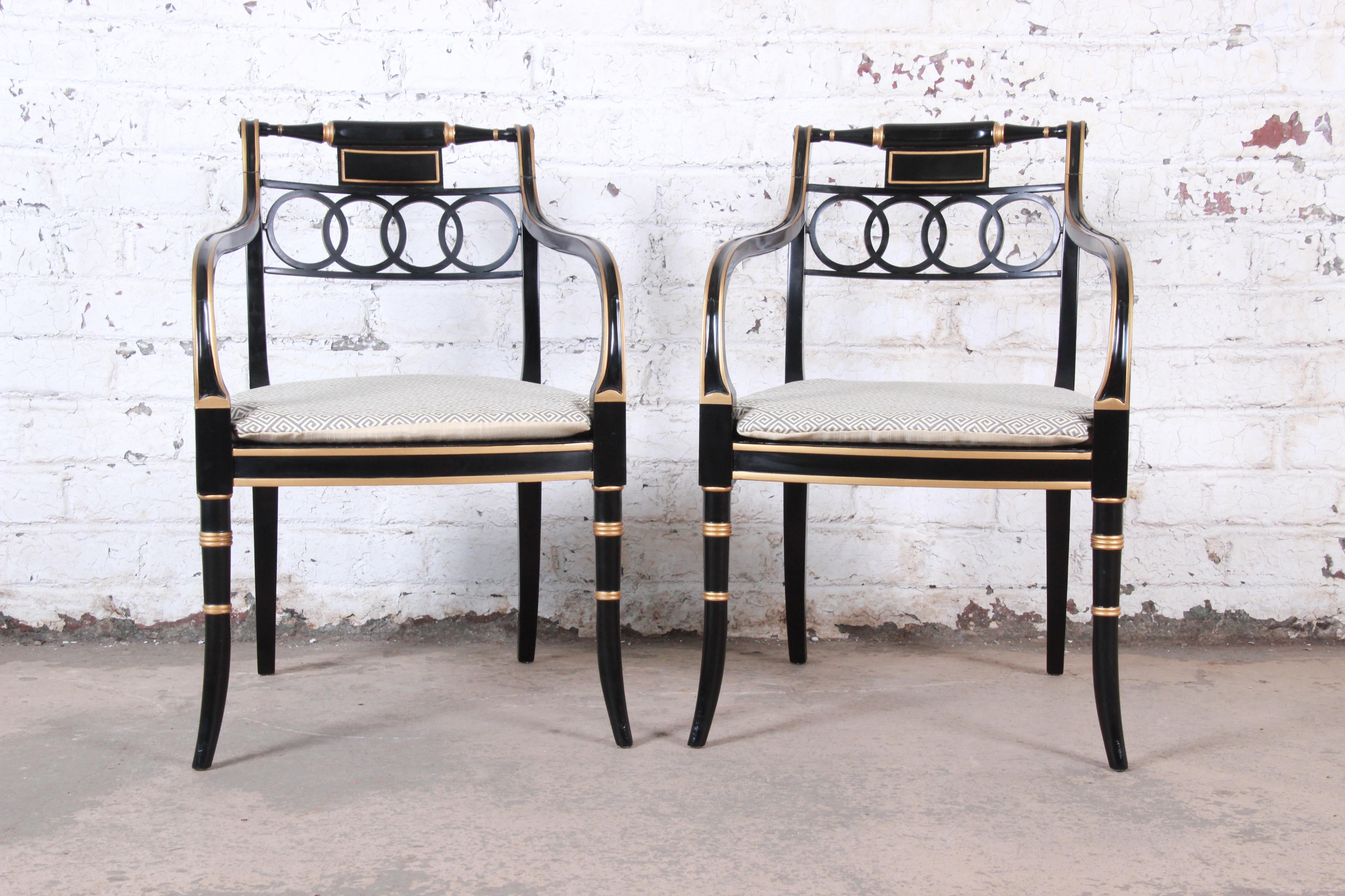 An exceptional pair of Regency style armchairs from the Historic Charleston collection by Baker Furniture. The chairs feature stunning ebonized and gold gilt solid wood frames with caned seats and removable seat cushions with Greek key design. Made