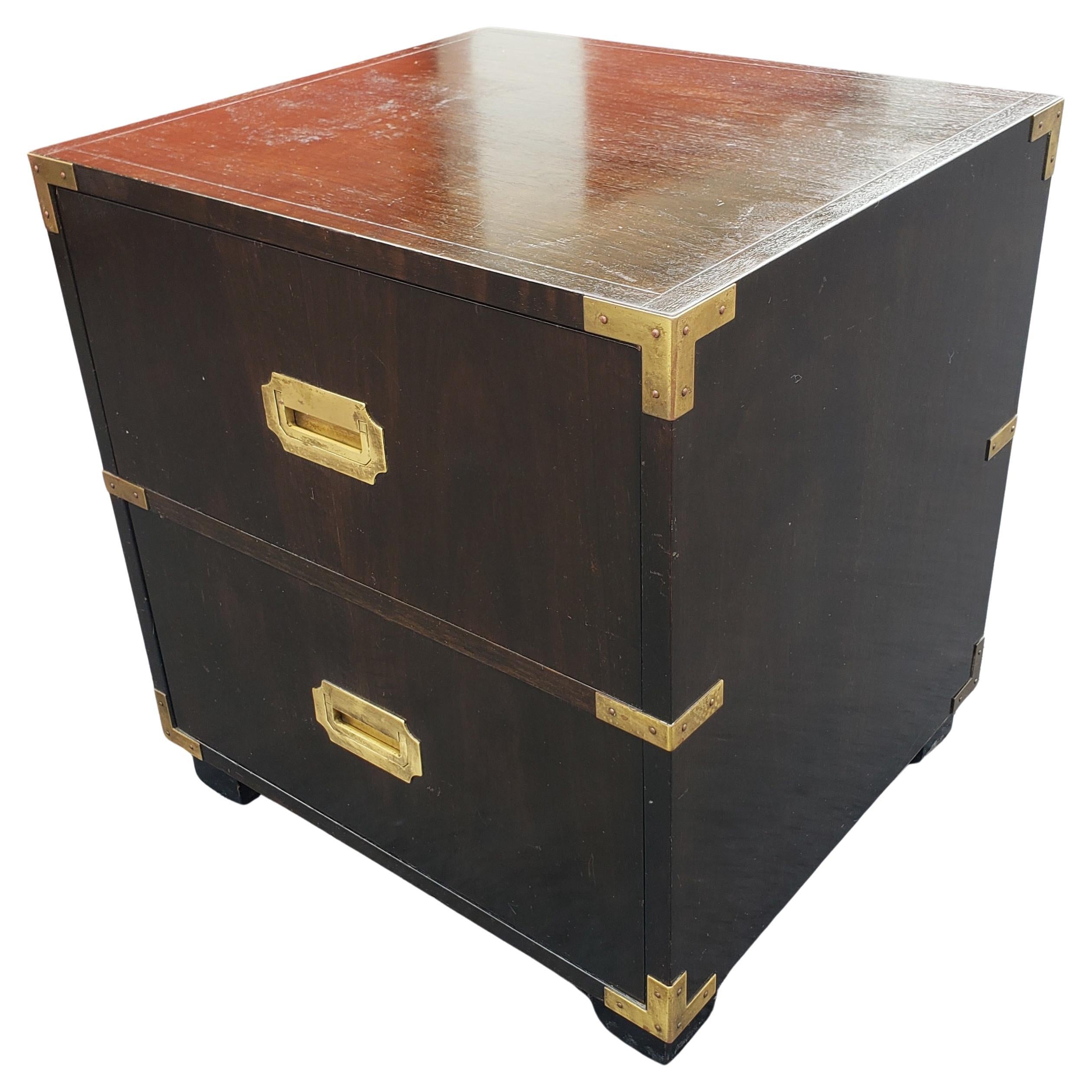 An exceptional Hollywood Regency Ebonized Campaign style nightstand or side table by Baker Furniture. The nightstand features gorgeous wood grain with original campaign brass hardware. It offers good storage, with a single dovetailed bottom drawer