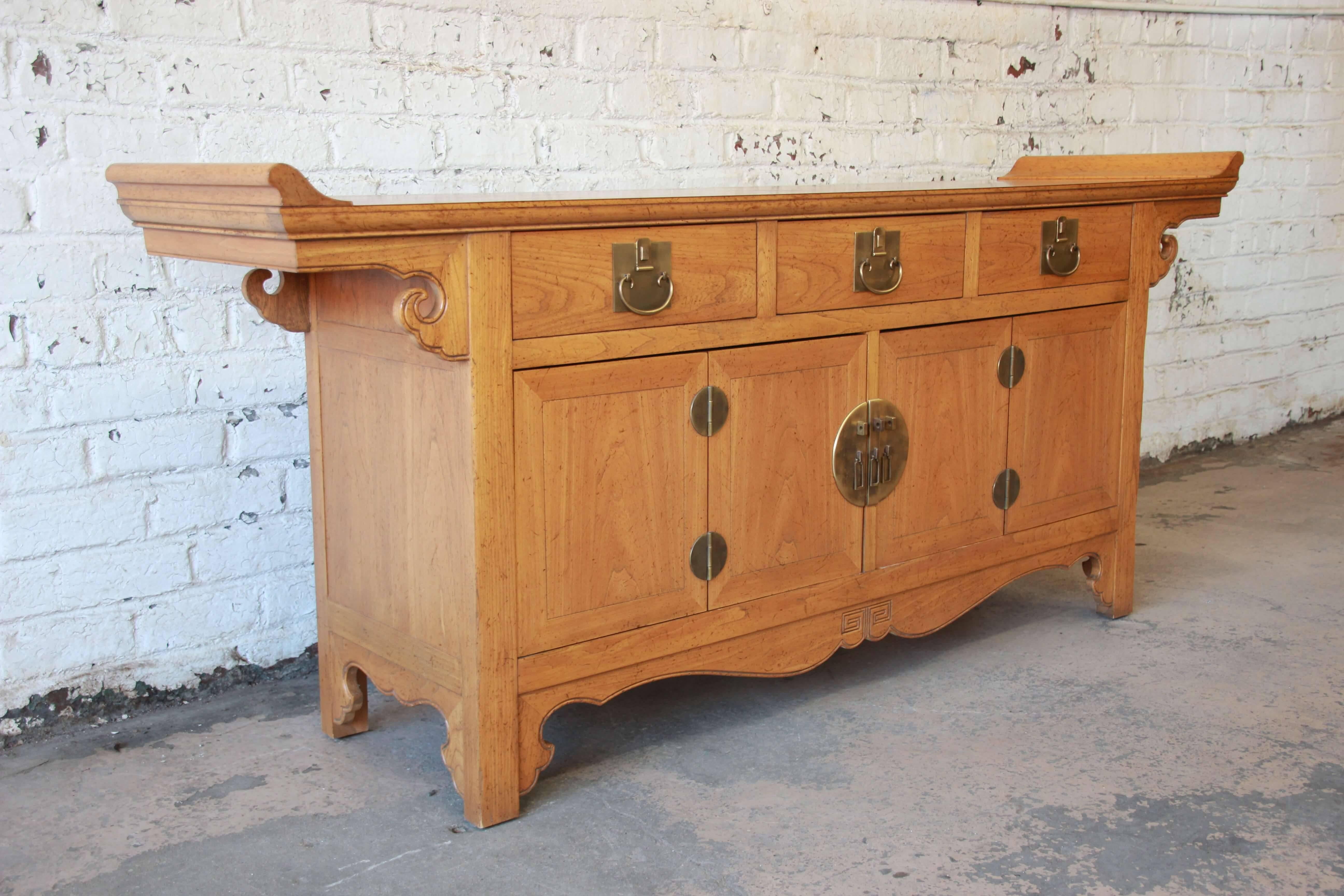 Offering a beautiful solid elmwood chinoiserie sideboard by Baker Furniture. This fantastic piece has brass hardware with Asian motifs and carvings. The top has elegant rolling edges with the piece featuring three large drawers directly below. Two