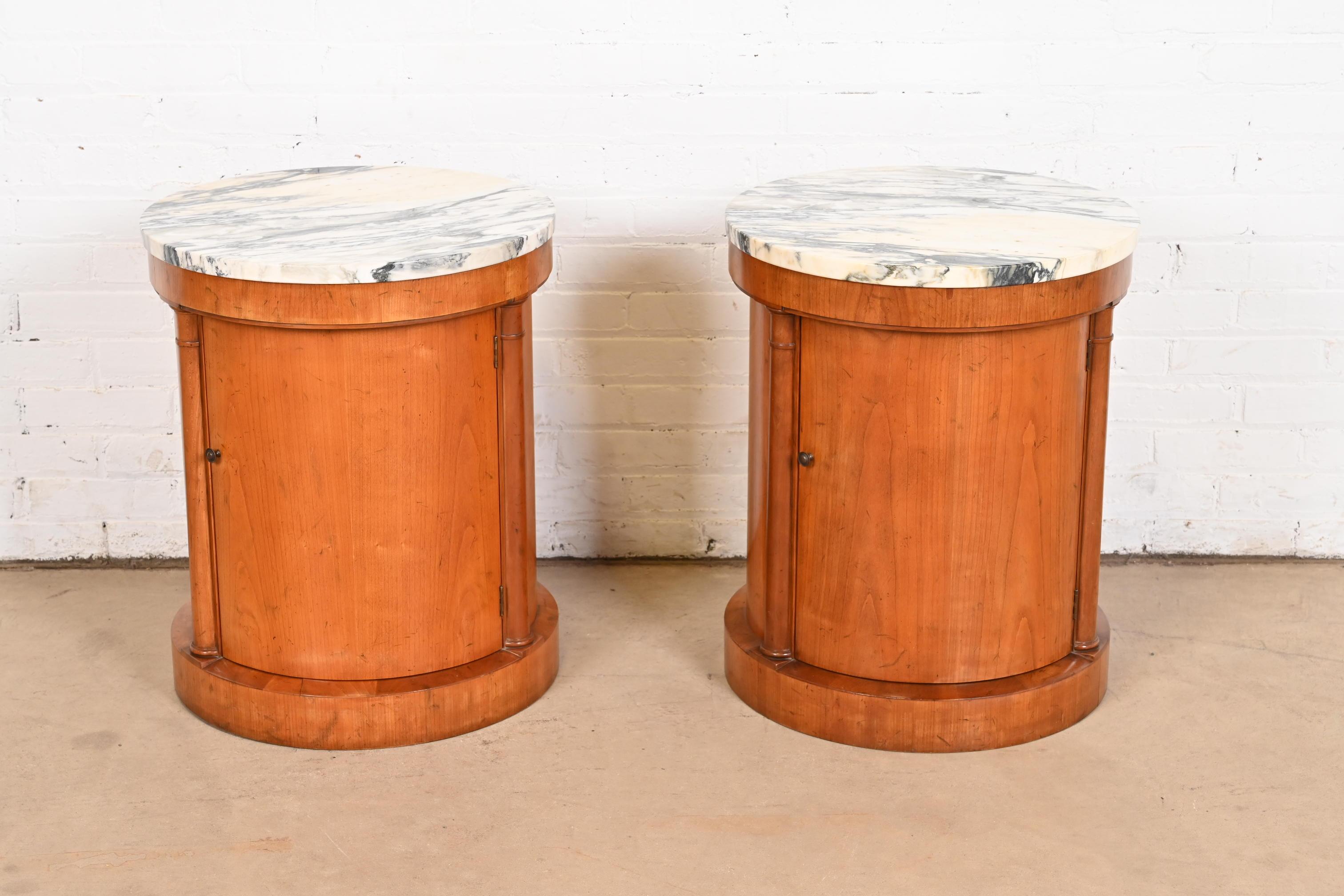 A gorgeous pair of Neoclassical or Empire style drum nightstands or side tables

By Baker Furniture

USA, Circa 1960s

Cherry wood, with Italian marble tops, and original brass hardware.

Measures: 20