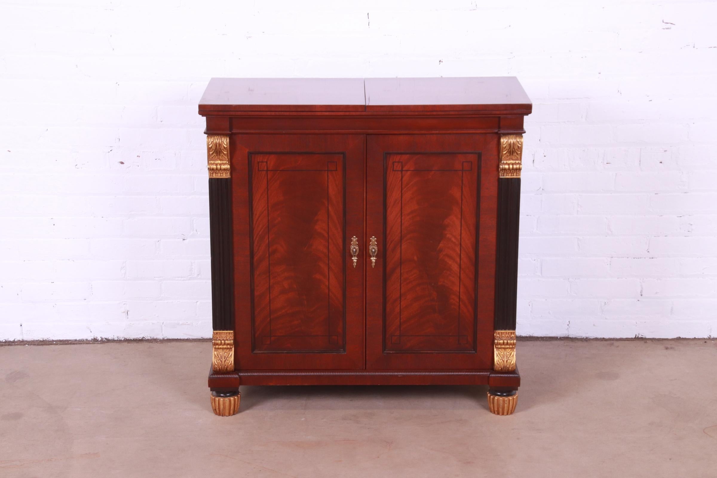 An exceptional Neoclassical or Empire style flip top server or bar cabinet.

By Baker Furniture

USA, Circa 1980s

Book-matched flame mahogany, with ebonized columns, gold gilt details, and original brass hardware.

Measures: 34