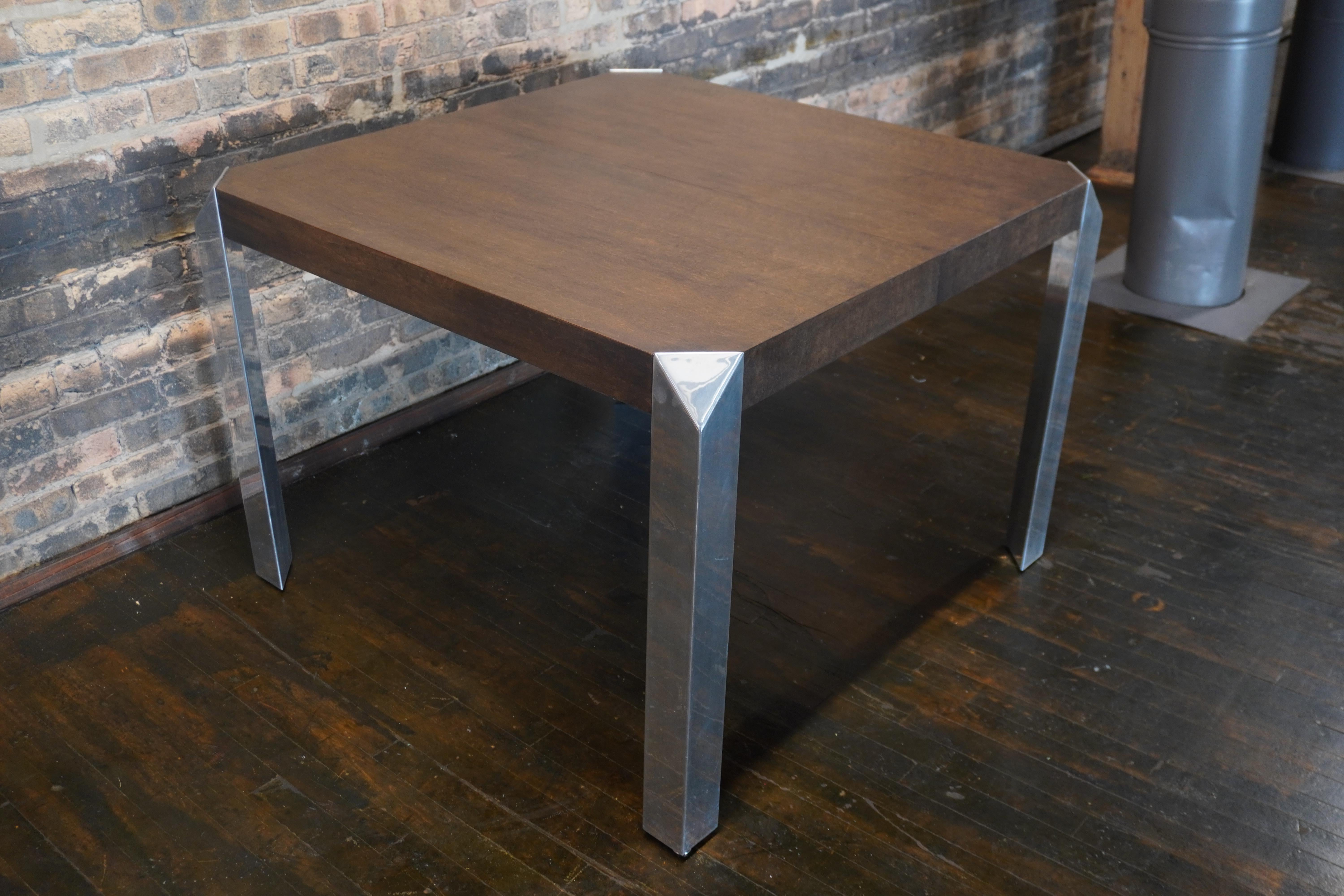 Stunning and unique mid-century dining table by Baker Furniture that features a walnut stained wood top and triangular shaped polished chrome legs (that add an architectural element to the piece). The table starts out as a square (40