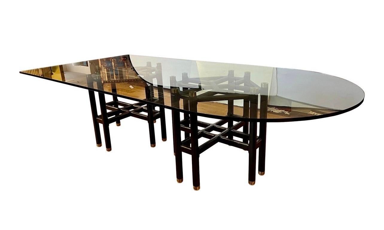 Stunning and one of a kind due to custom sculptural glass top dining table with two Baker Furniture octagonal pedestal bases that are ebonized in black and gold.  The glass top has a unique boat shape as shown.  Note that glass stills on the two
