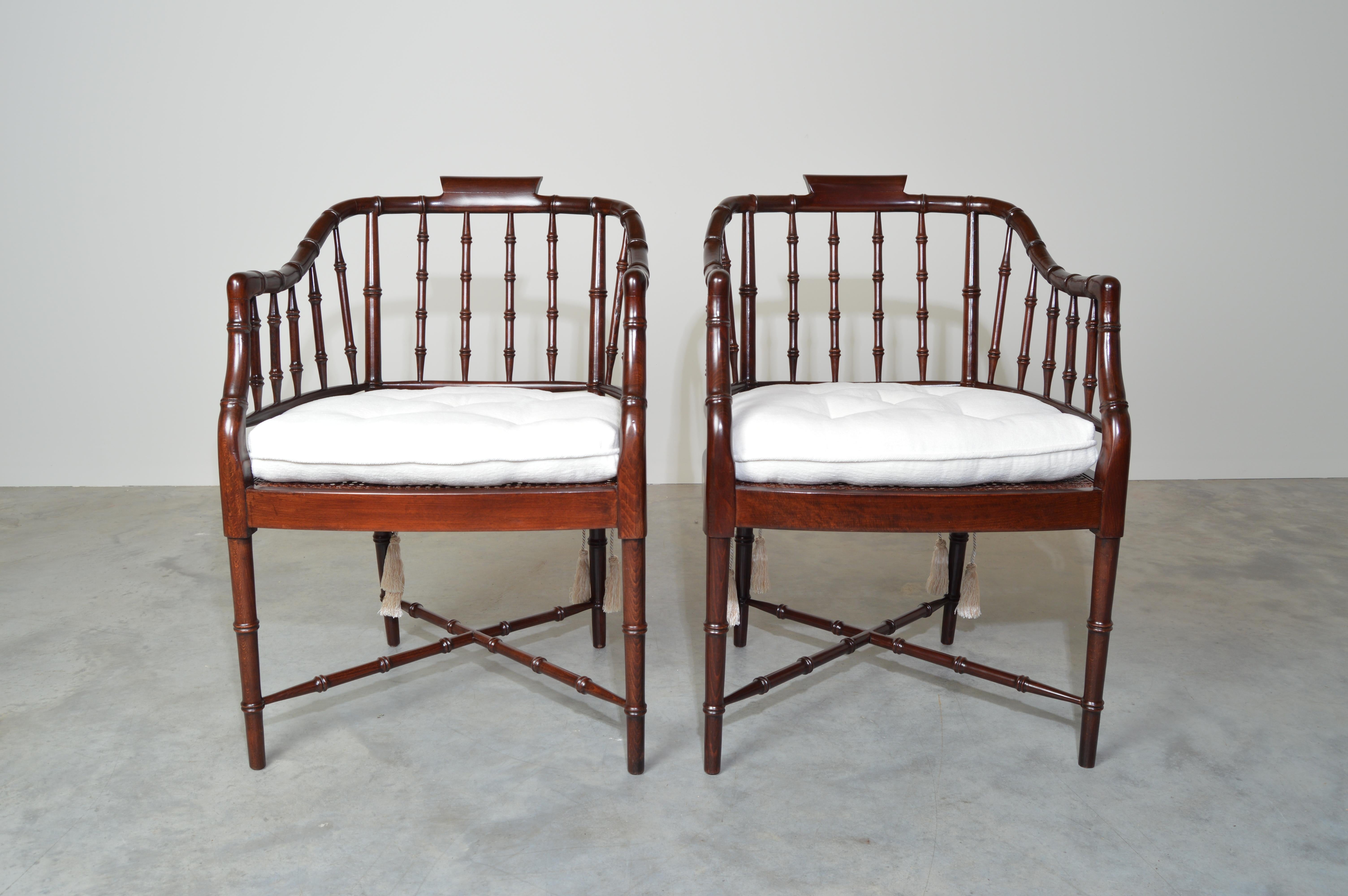 A beautiful pair of faux bamboo Regency armchairs having new caned seats by Baker Furniture USA, 1960s. Includes custom tufted subtly off-white Italian boucle' cushions with tassel ties. Excellent vintage condition. 
Seat height 20