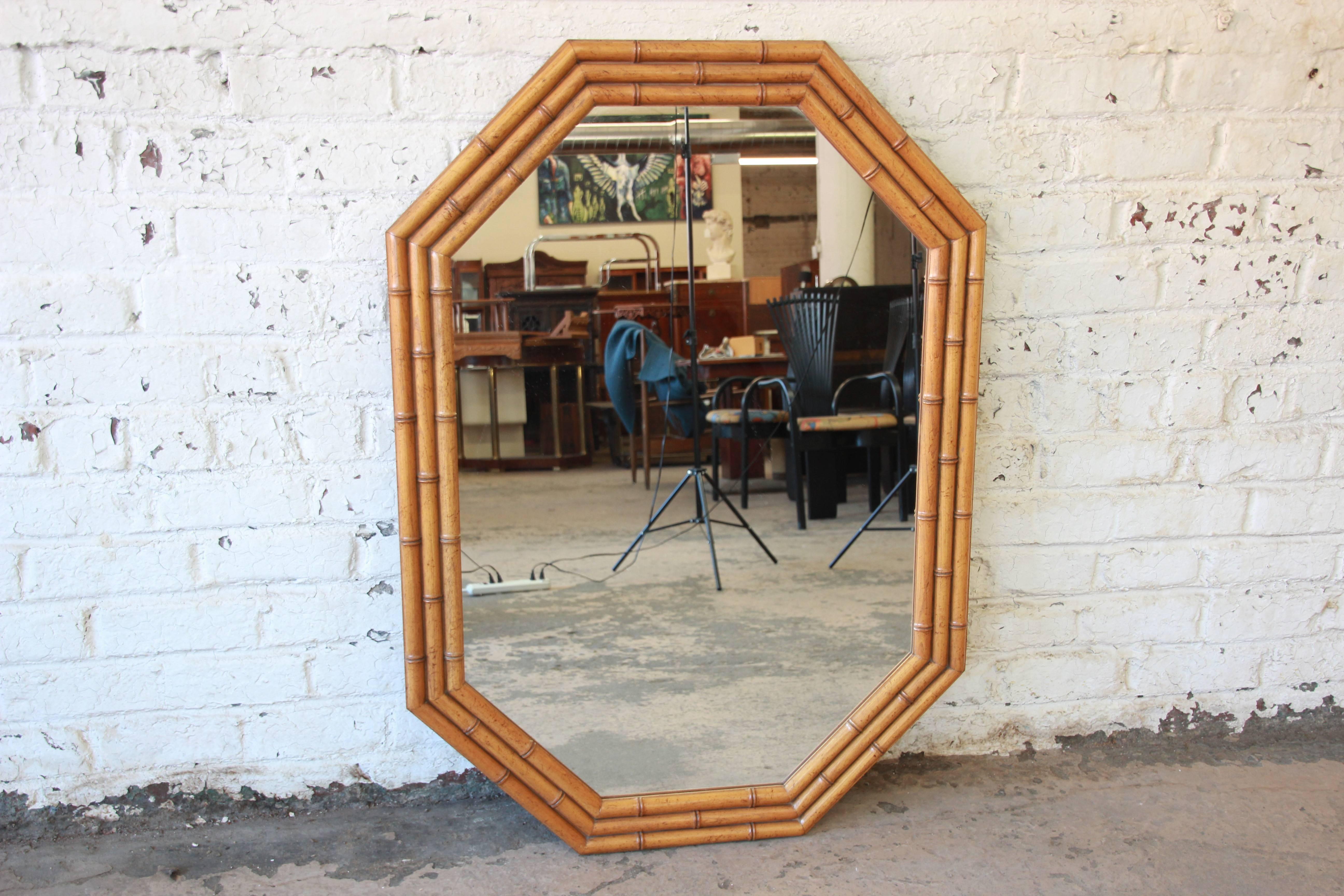 An outstanding faux bamboo Hollywood Regency chinoiserie mirror by Baker Furniture. The mirror features three bands of carved faux bamboo in elmwood in an octagonal shape. The metal Baker Furniture label is present on the backside. The mirror is in