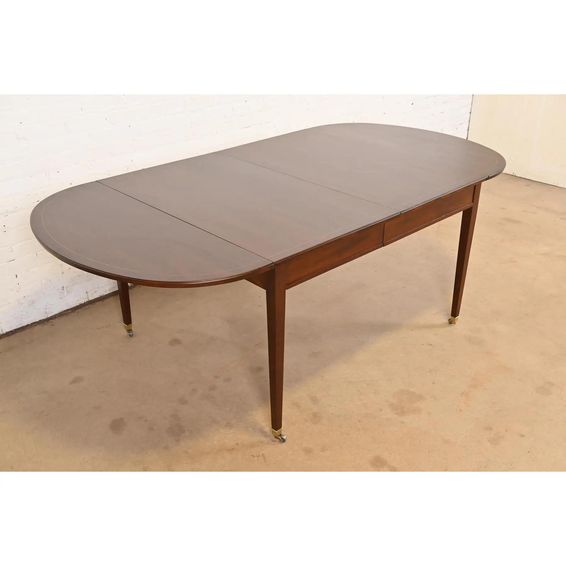 Una magnífica mesa de comedor de hojas abatibles de estilo Federal o Regencia

Por Baker Furniture

EE.UU., alrededor de 1980

Preciosa caoba bandeada a juego con el libro, con incrustaciones de cuerda de madera satinada, y pies con tapa de latón