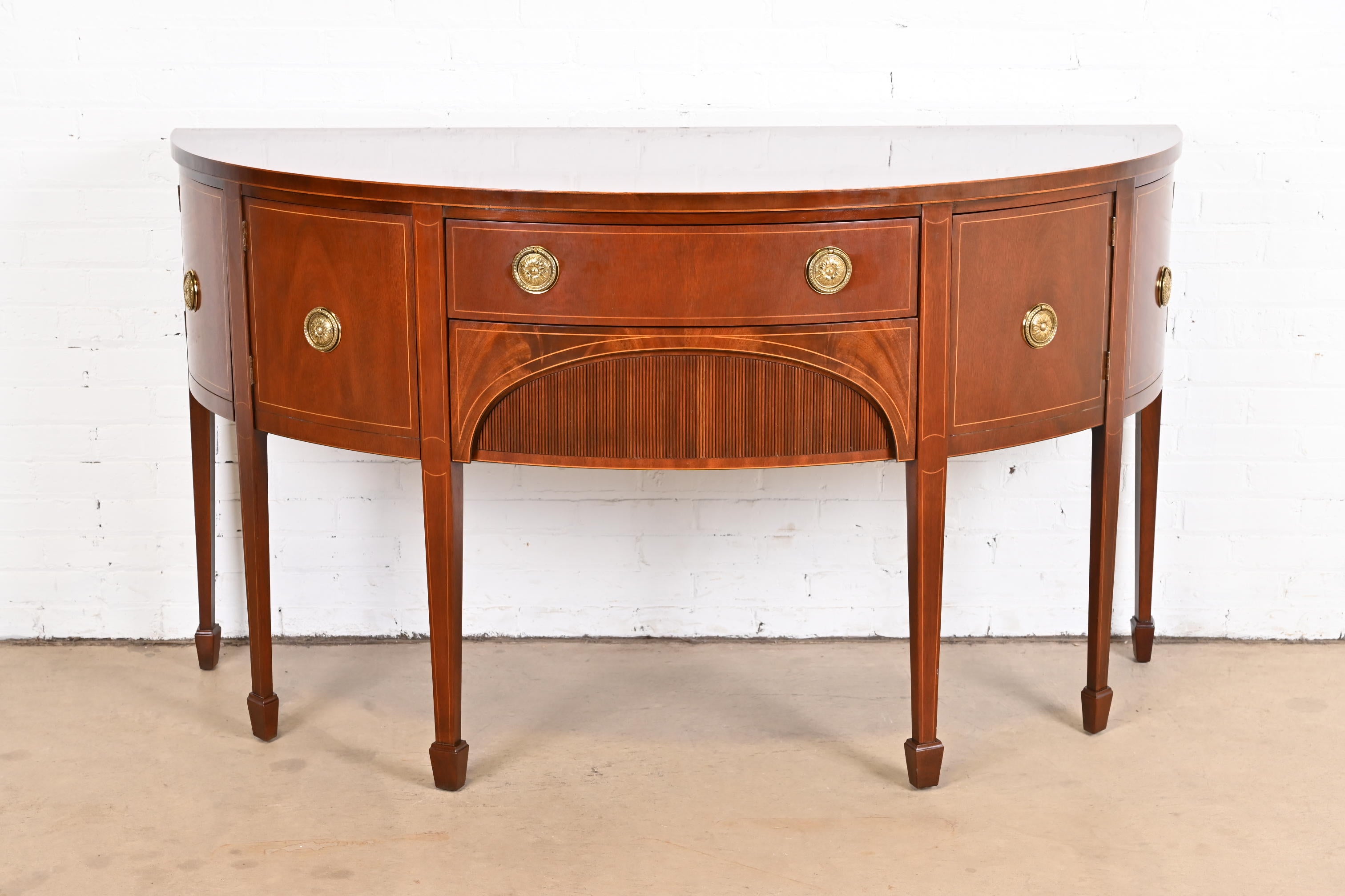 A beautiful Federal or Hepplewhite style demilune cabinet or sideboard

By Baker Furniture

USA, circa 1980s

Mahogany, with satinwood string inlay, original brass hardware, and felt silverware insert.

Measures: 66