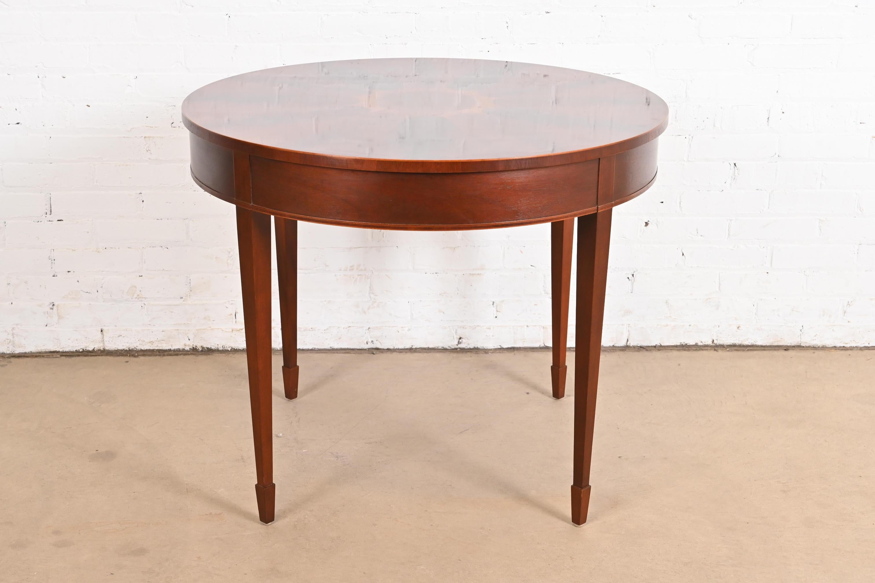 A gorgeous Federal or Hepplewhite style  dining table, center table, game table, or breakfast table

By Baker Furniture

USA, Late 20th Century

Gorgeous book-matched flame mahogany in starburst pattern, with satinwood inlay.

Measures: 36