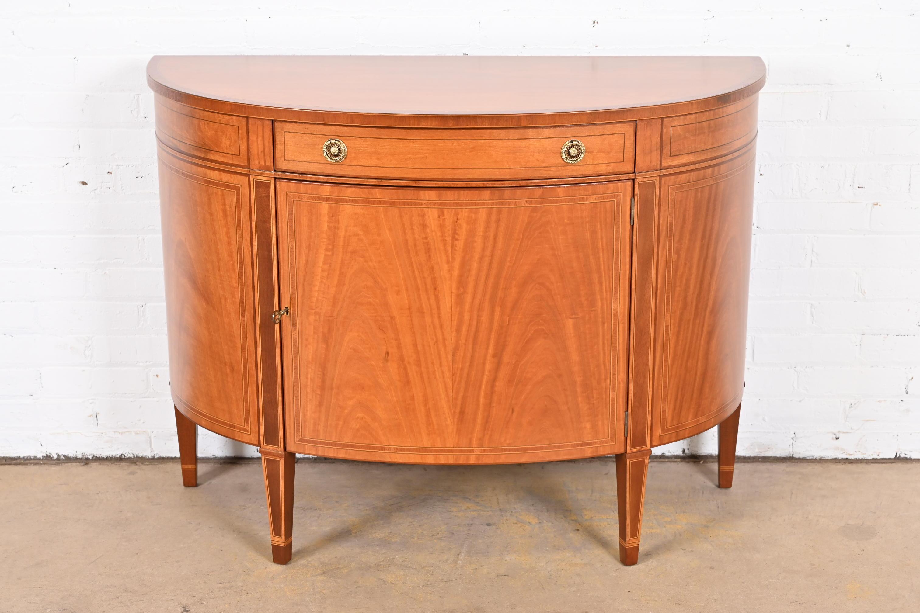 An exceptional Federal style demilune sideboard or bar cabinet

By Baker Furniture

USA, Circa 1980s

Mahogany and satinwood, with original brass hardware. Cabinet locks, and key is included.

Measures: 43