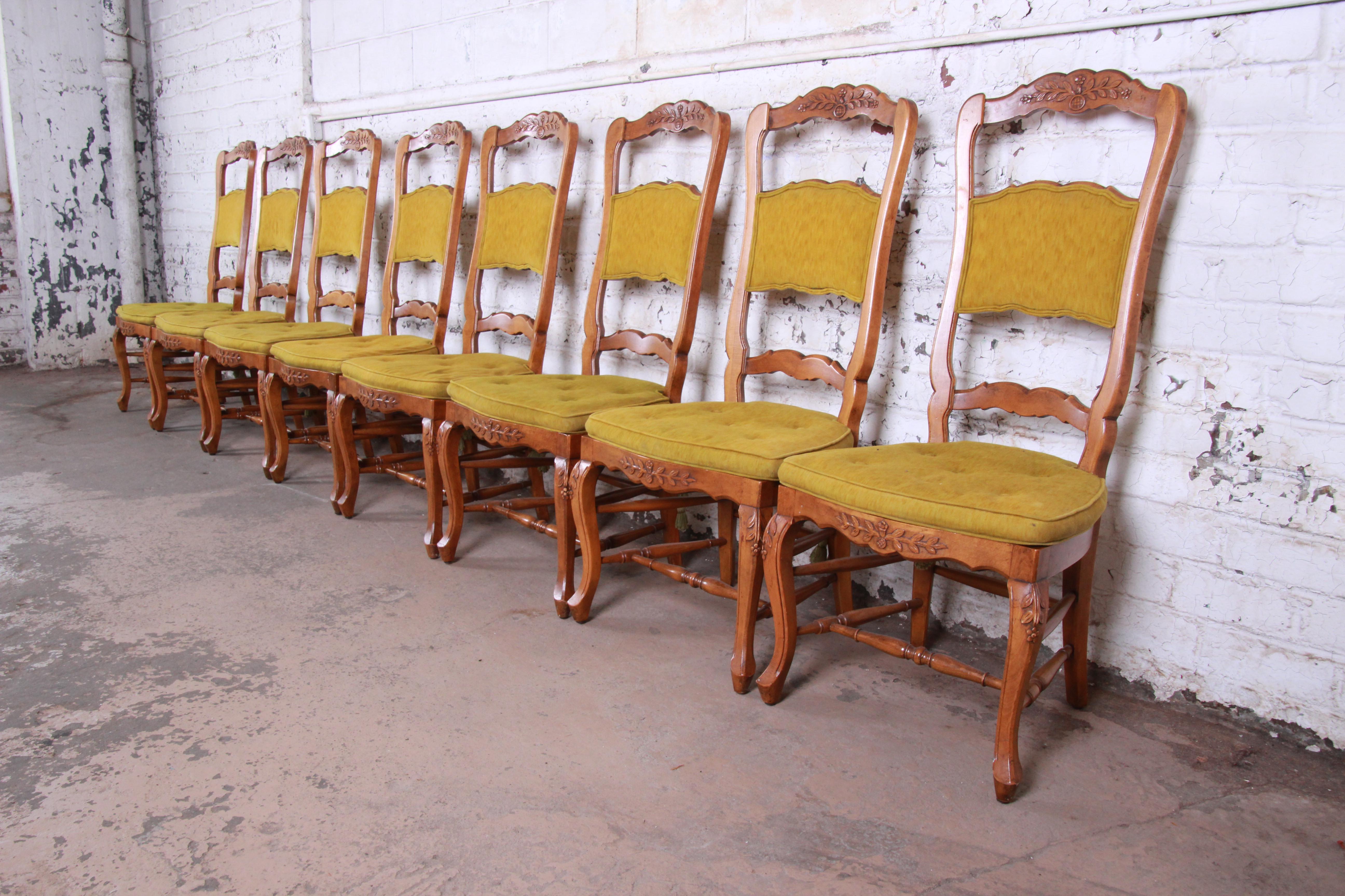 A beautiful set of eight country French high back dining chairs by Baker Furniture. The chairs feature solid wood frames, with nice floral carved wood details and tall ladder backs. They have tufted green upholstered seat cushions and upholstered