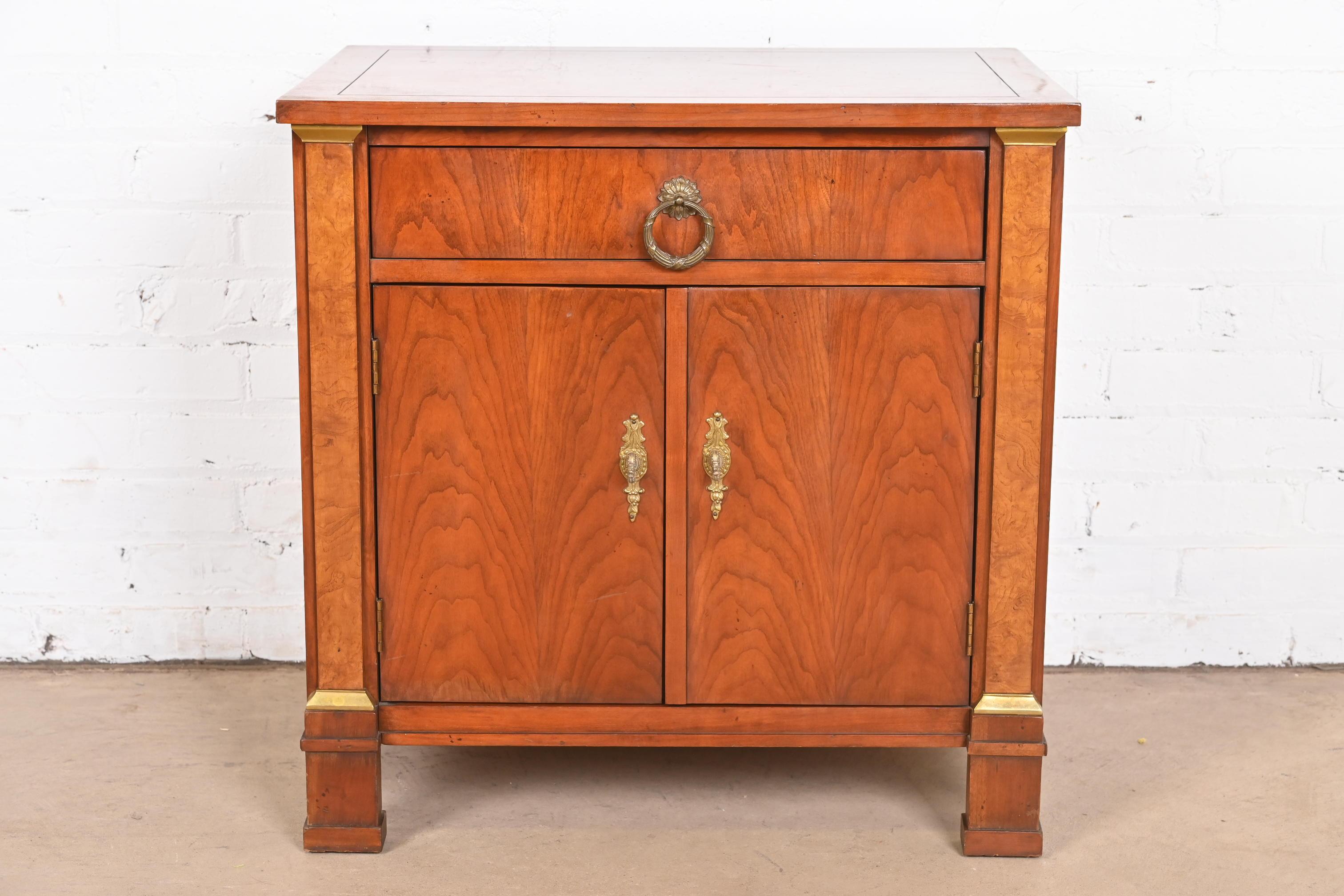 A gorgeous French Empire or Neoclassical style nightstand or end table

By Baker Furniture

USA, Circa 1980s

Beautiful book-matched cherry wood, with burl wood columns and original brass hardware.

Measures: 25