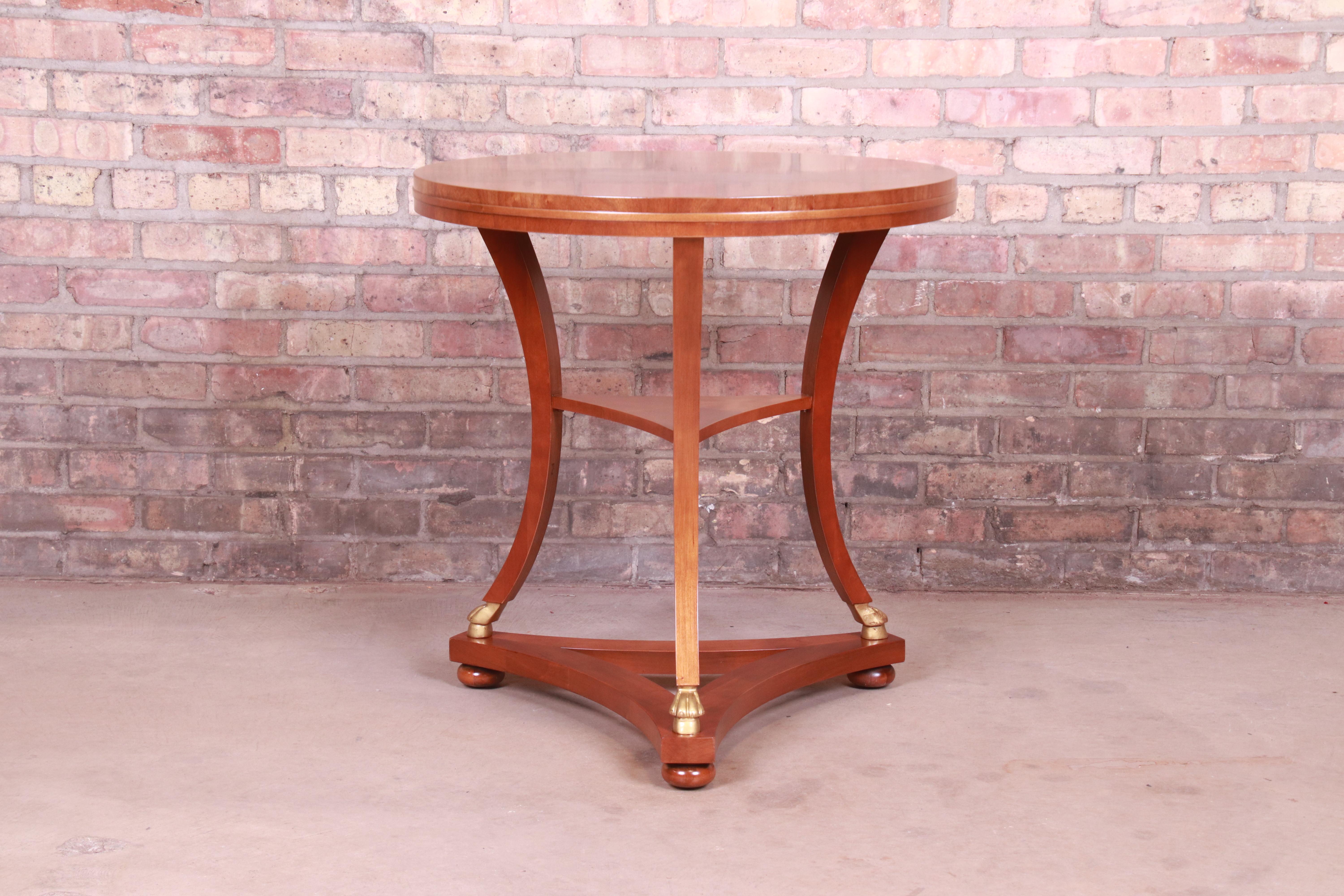 A gorgeous French Empire or neoclassical style tea table or occasional side table

By Baker Furniture

USA, circa 1980s

Book-matched mahogany in starburst pattern, with gold gilt paw feet.

Measures: 26