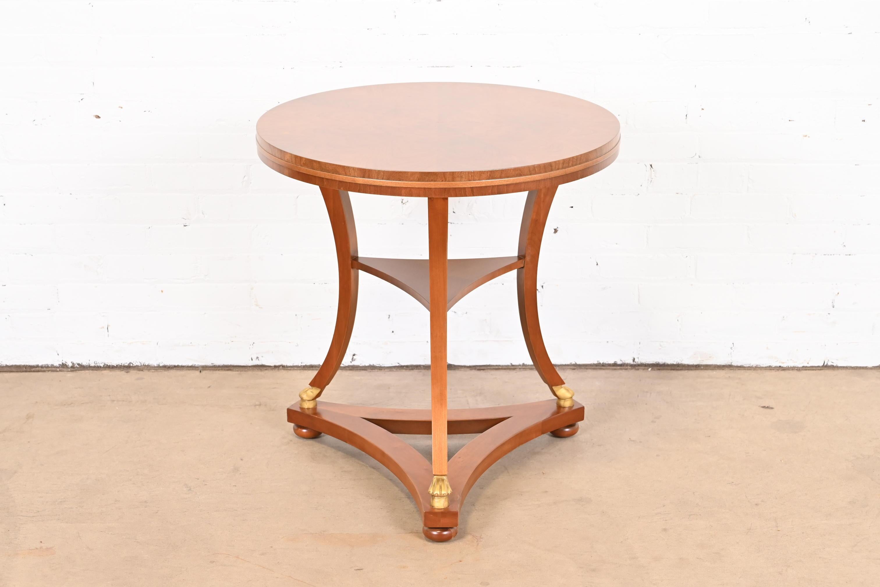 A gorgeous French Empire or Neoclassical style tea table or occasional side table

By Baker Furniture

USA, Circa 1980s

Book-matched mahogany in starburst pattern, with gold gilt paw feet.

Measures: 26