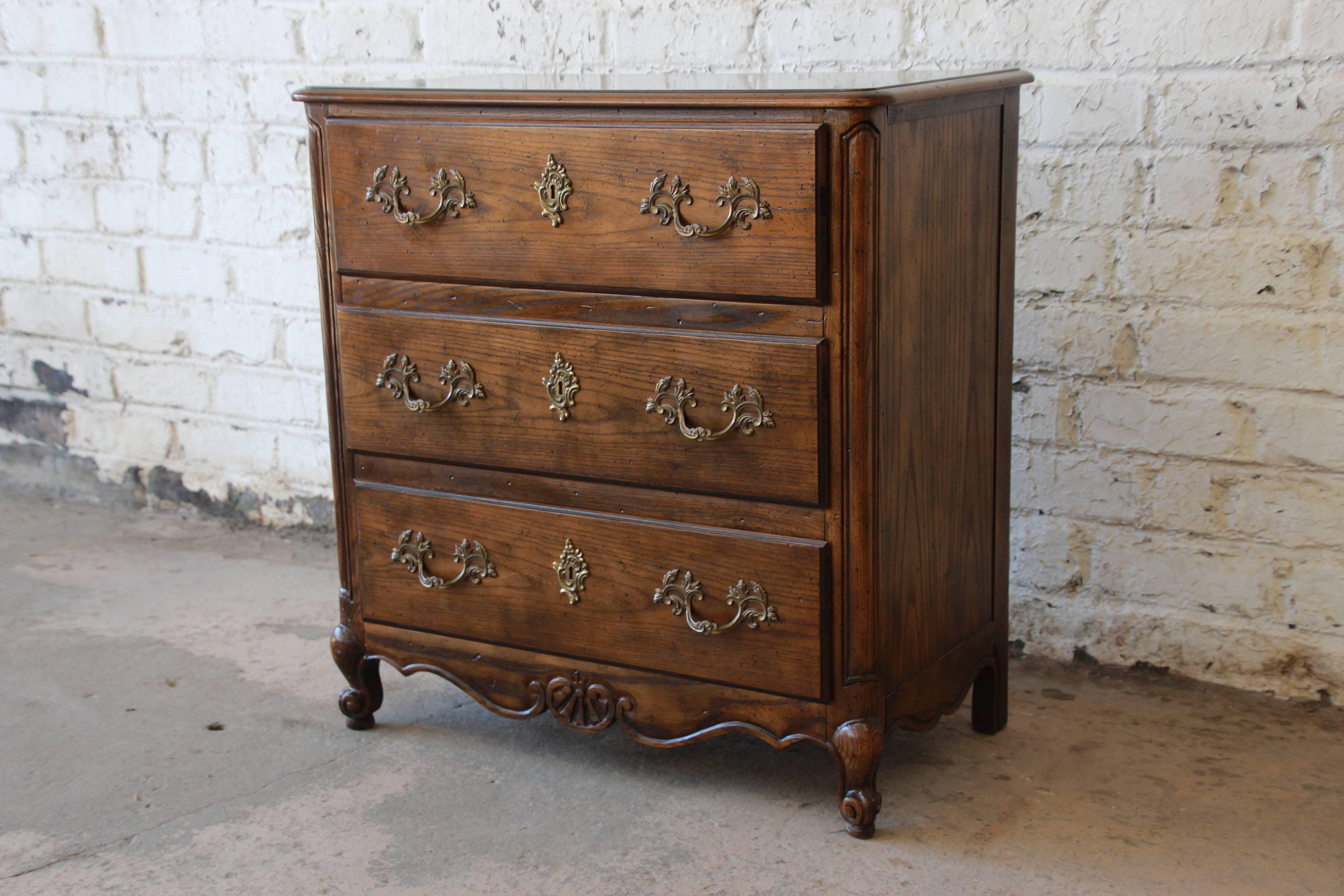 A beautiful vintage three-drawer chest in Louis XV style by Baker Furniture. The chest features gorgeous wood grain and an inlaid burl wood top. It is well constructed from solid oak and offers good storage with three dovetailed drawers. The