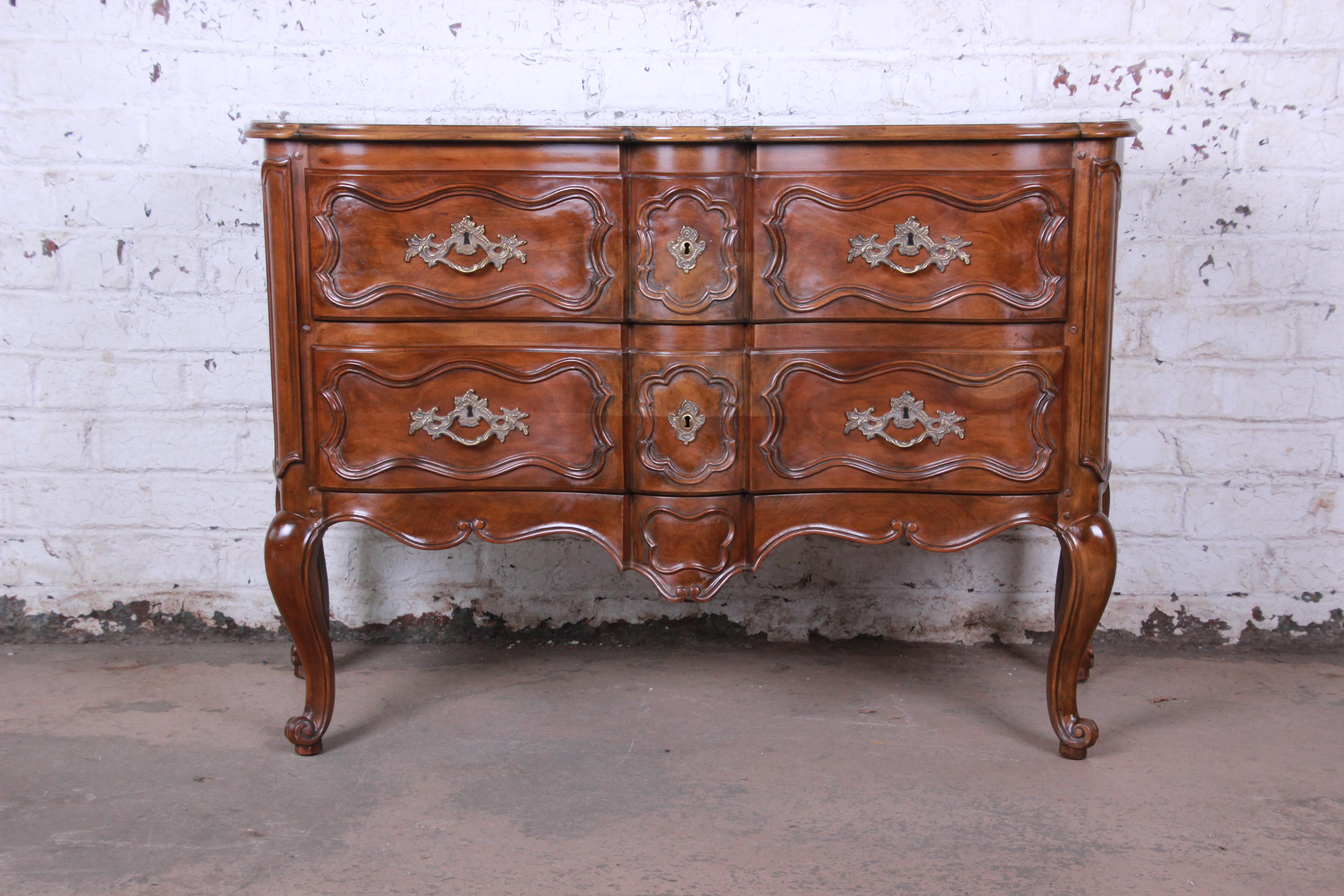 A gorgeous French Louis XV style sideboard server or commode by Baker Furniture. The commode features nice French carved details and beautiful walnut wood grain. It offers good storage, with two deep dovetailed drawers. Brass hardware is original. A