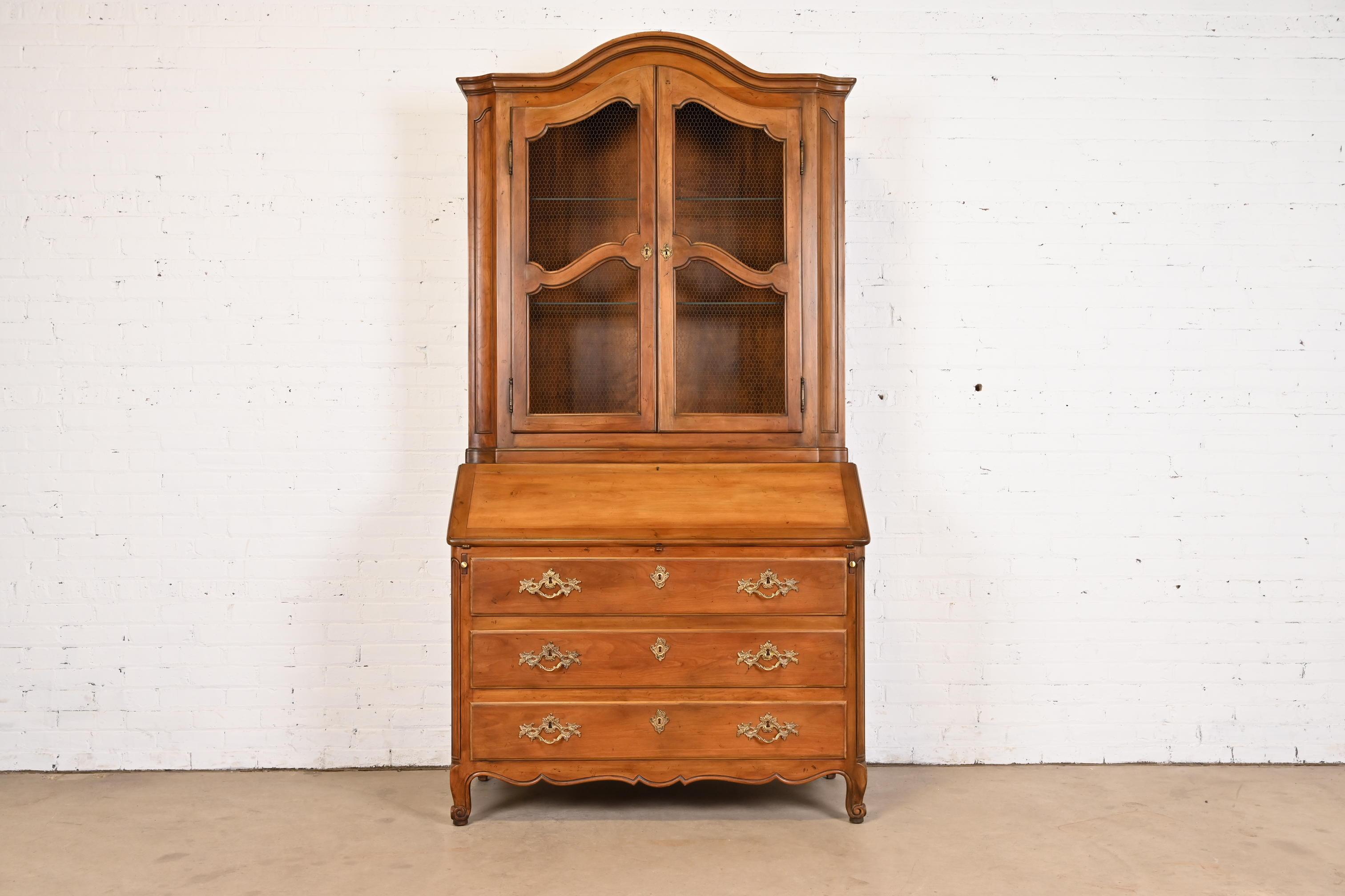 A gorgeous French Provincial Louis XV style bureau with drop front secretary desk and lighted bookcase hutch top

By Baker Furniture

USA, Circa 1960s

Carved walnut, with original brass hardware, and leather writing surface. Cabinet locks, and