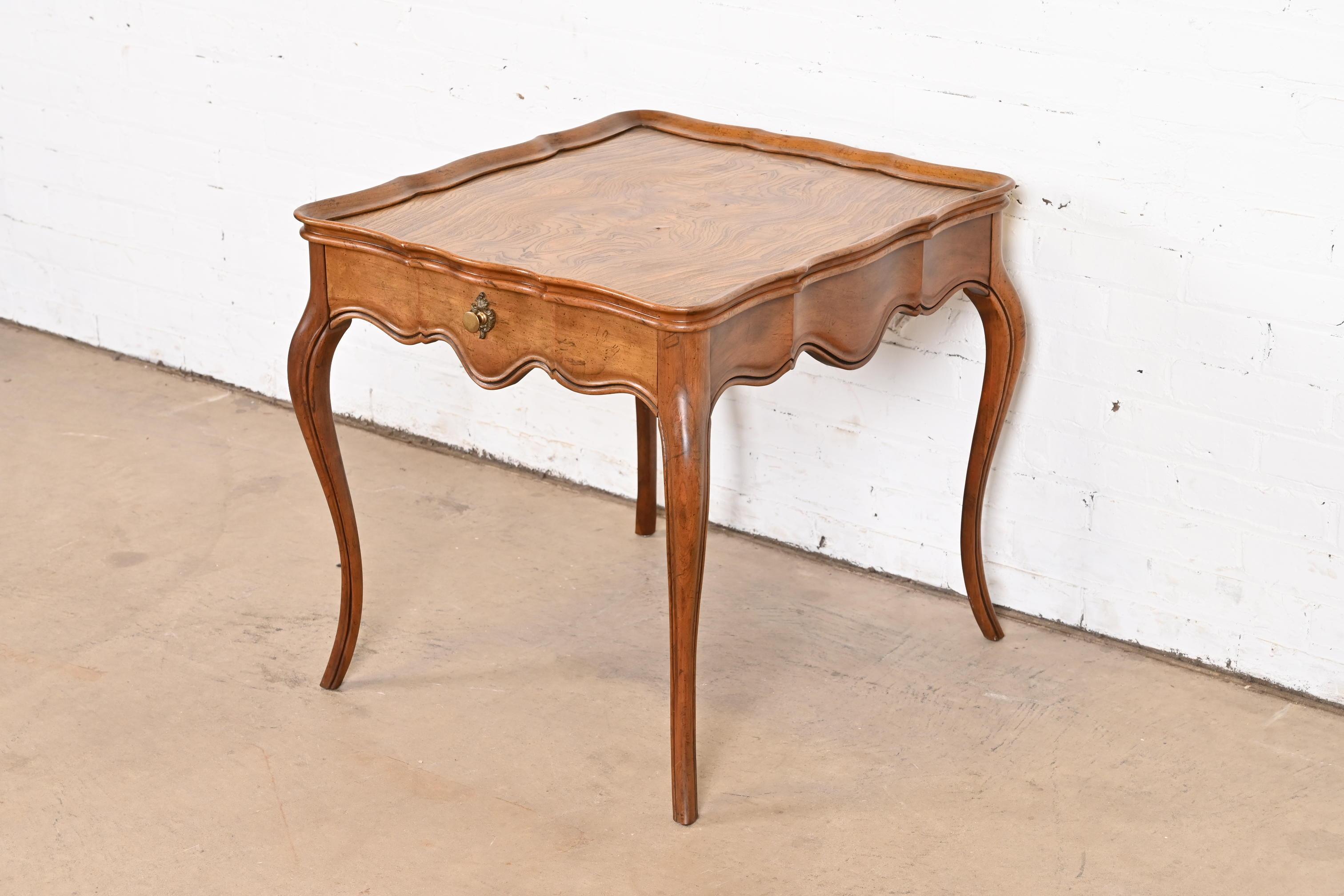 A beautiful French Provincial Louis XV style one-drawer nightstand, tea table, or occasional side table

By Baker Furniture

USA, Circa 1960s

Carved cherry wood, with gorgeous book-matched burl wood top, and original brass hardware.

Measures: