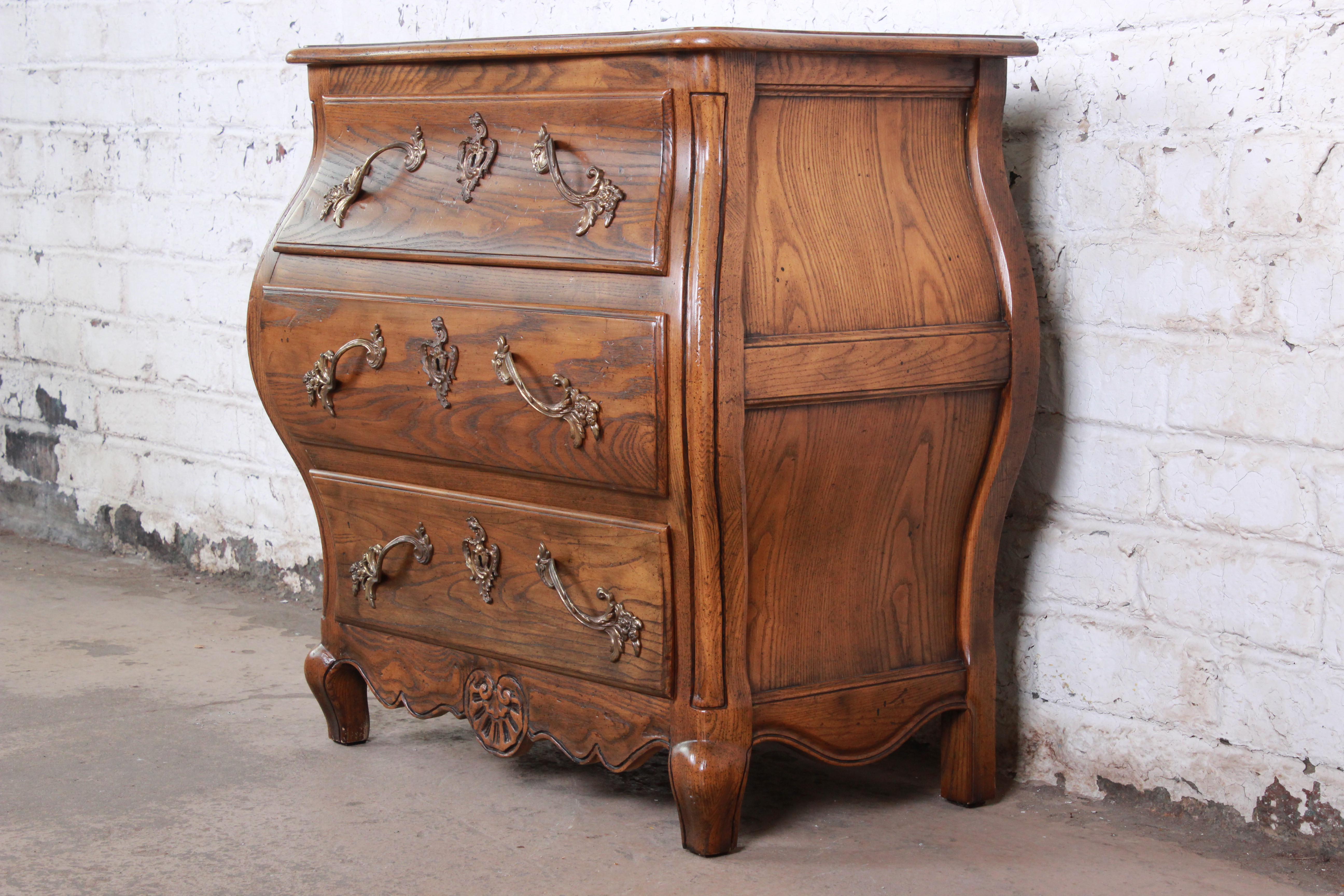 An exceptional French Provincial Louis XV style commode or bombay chest by Baker Furniture. The chest features solid oak construction, with beautiful wood grain and nice carved details. It offers good storage, with three deep dovetailed drawers.