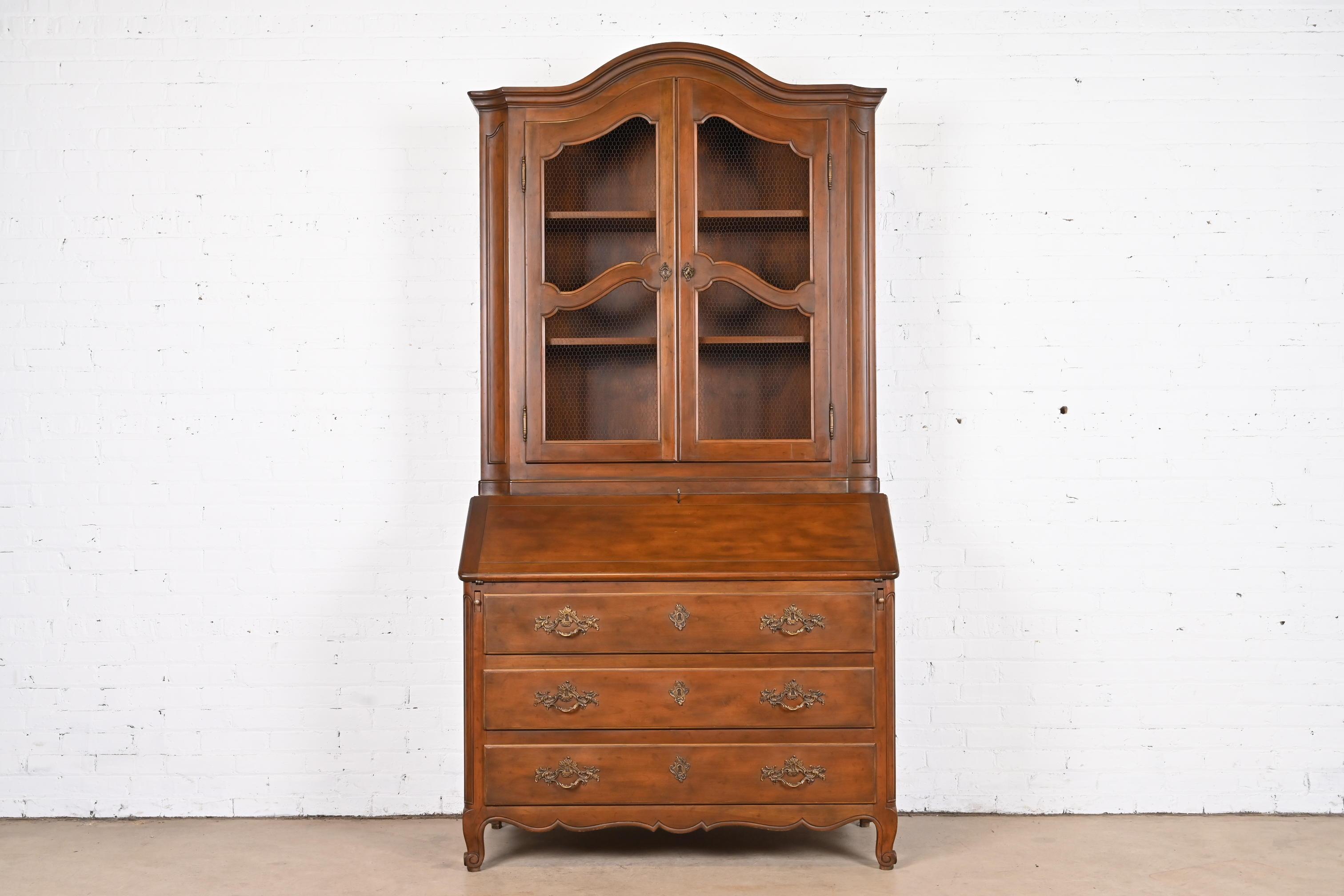 A gorgeous French Provincial Louis XV style bureau with drop front secretary desk and bookcase hutch top

By Baker Furniture

USA, Circa 1960s

Carved walnut, with original brass hardware, and leather writing surface. Cabinet locks, and