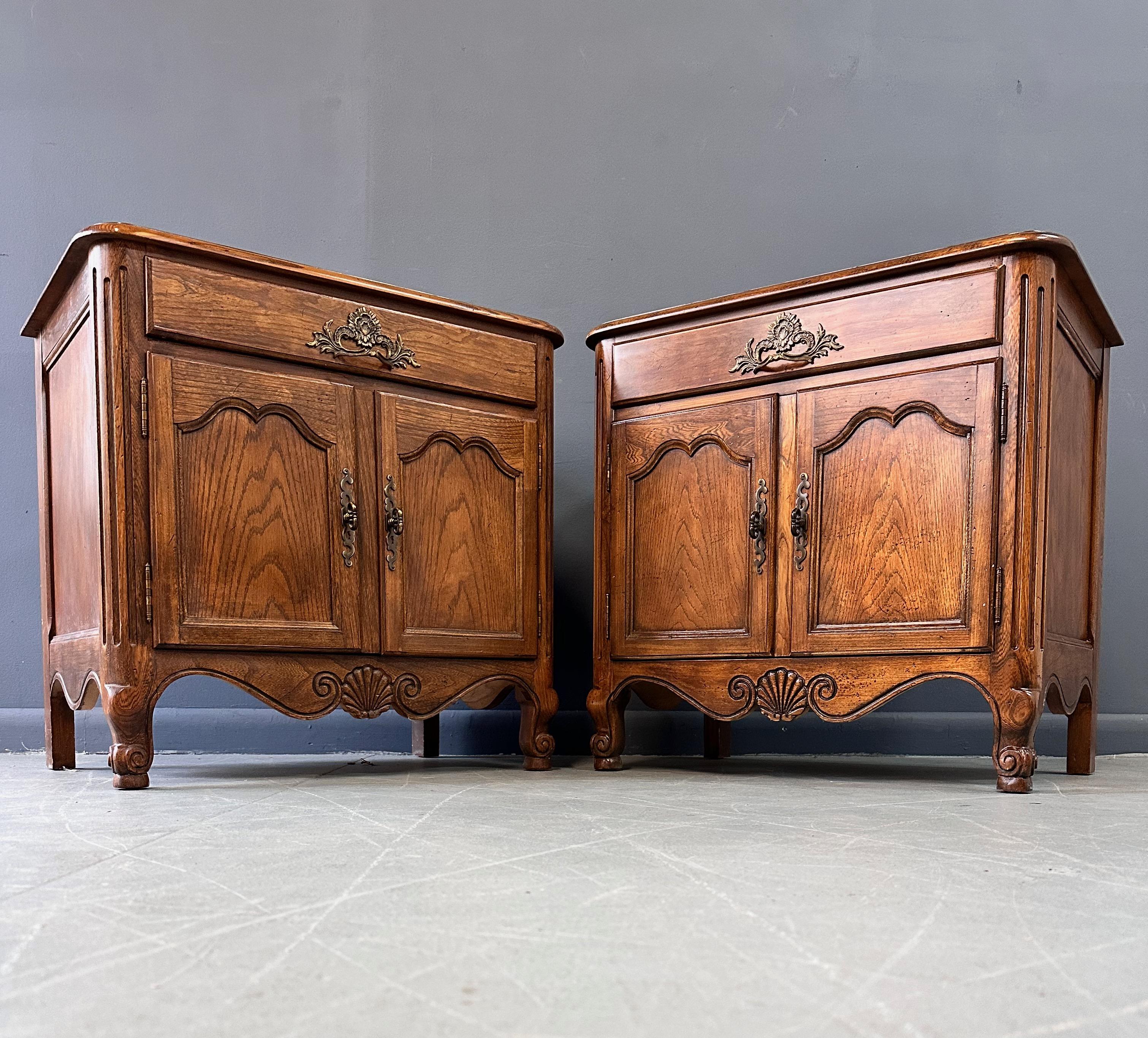 Wonderful and solid Baker nightstands in oak styled in a lovely French provincial motif. These stands have one drawer on top and two doors underneath with a good amount of space. These nightstands have been outfitted with an electrical plug on the
