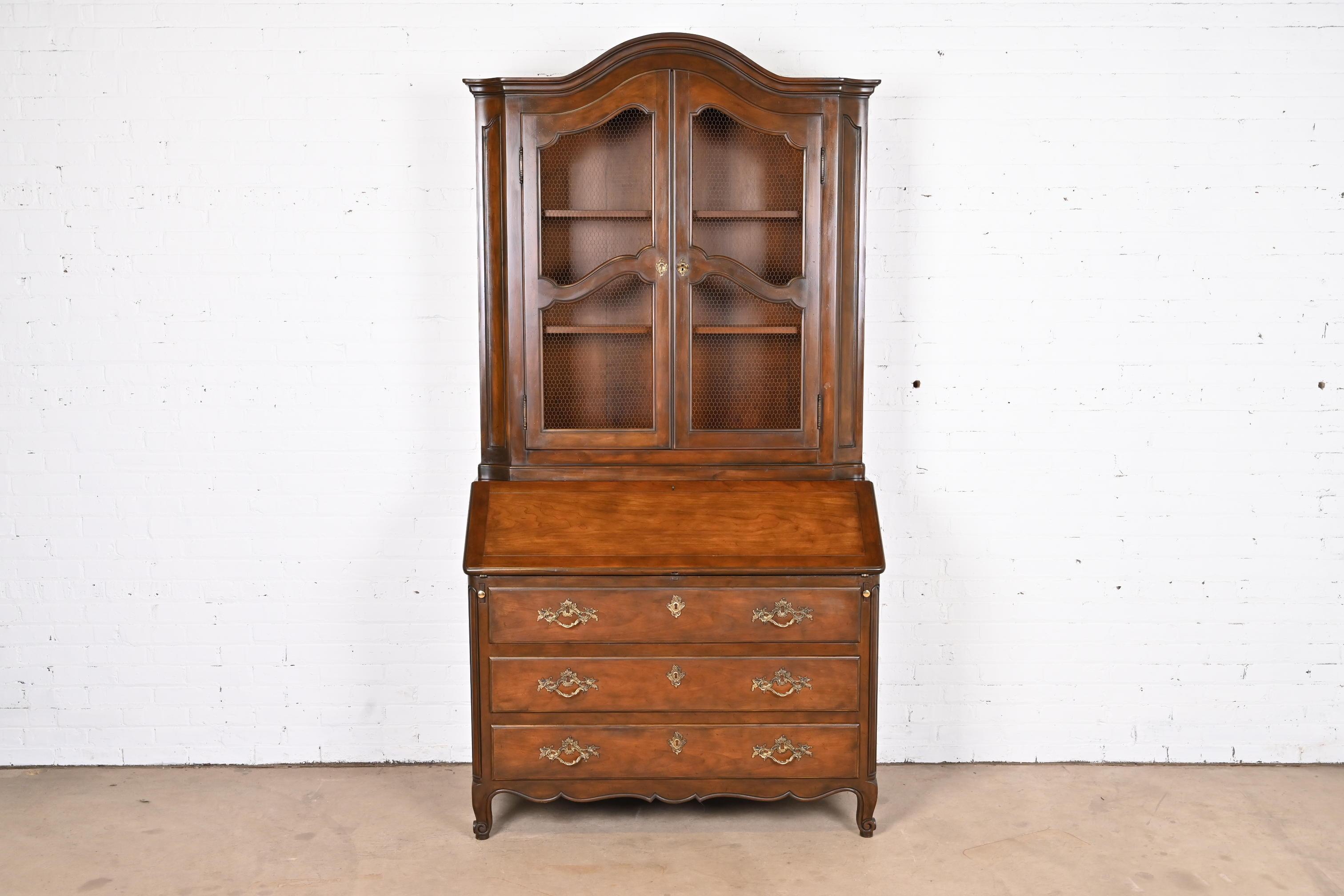 A gorgeous French Provincial Louis XV style bureau with drop front secretary desk and bookcase hutch top

By Baker Furniture

USA, Circa 1960s

Carved walnut, with original brass hardware, and leather writing surface. Cabinet locks, and original key