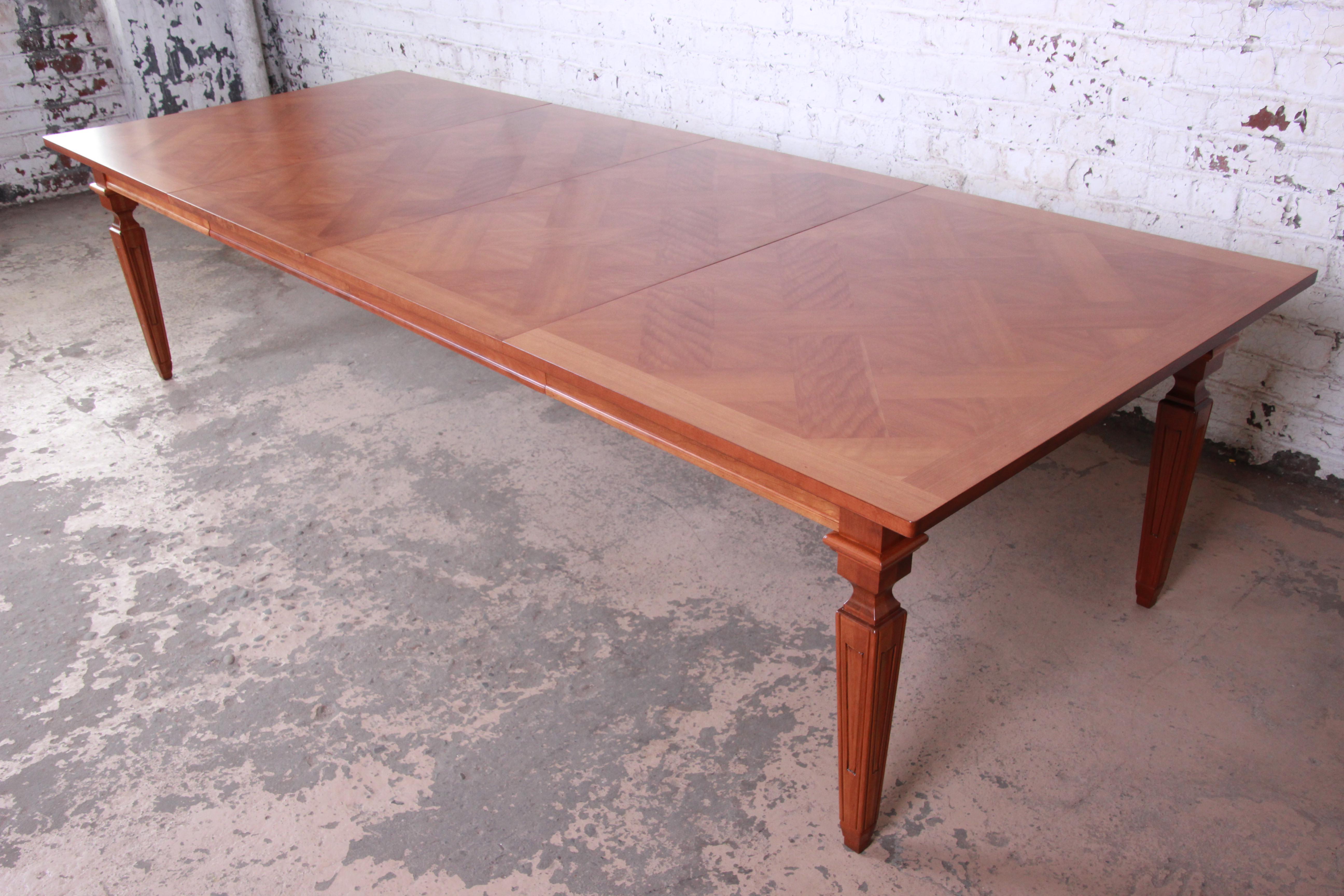 A gorgeous newly restored French Regency extension dining table by Baker Furniture. The table features a nice parquetry top and beautiful cherrywood grain. With two large 26.5
