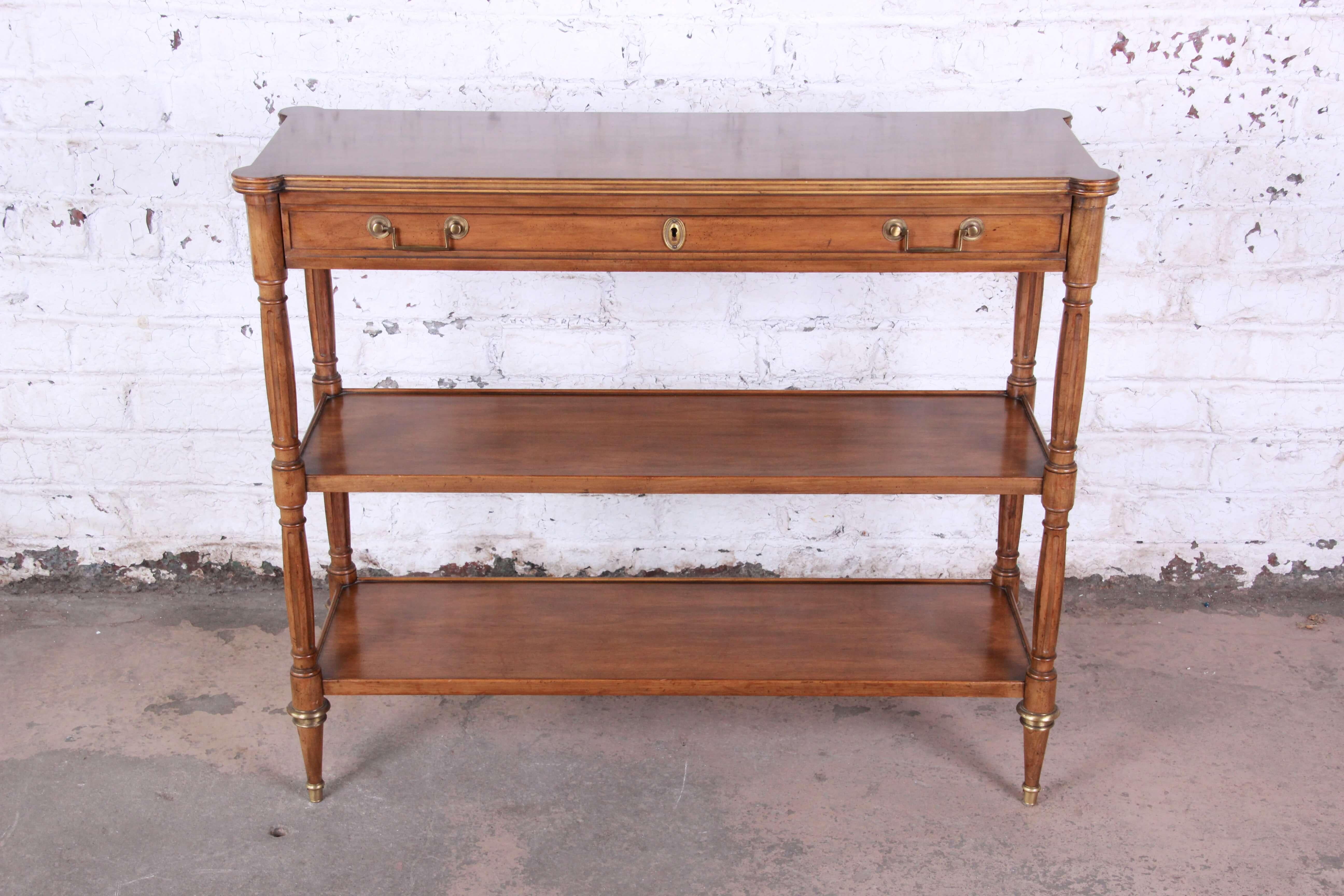 Offering a very nice Baker Furniture French Regency style bar serve or console table. The piece has a nice three-tier feature along with a large locking drawer. It has solid brass details displaying it quality and attention to detail. The piece is
