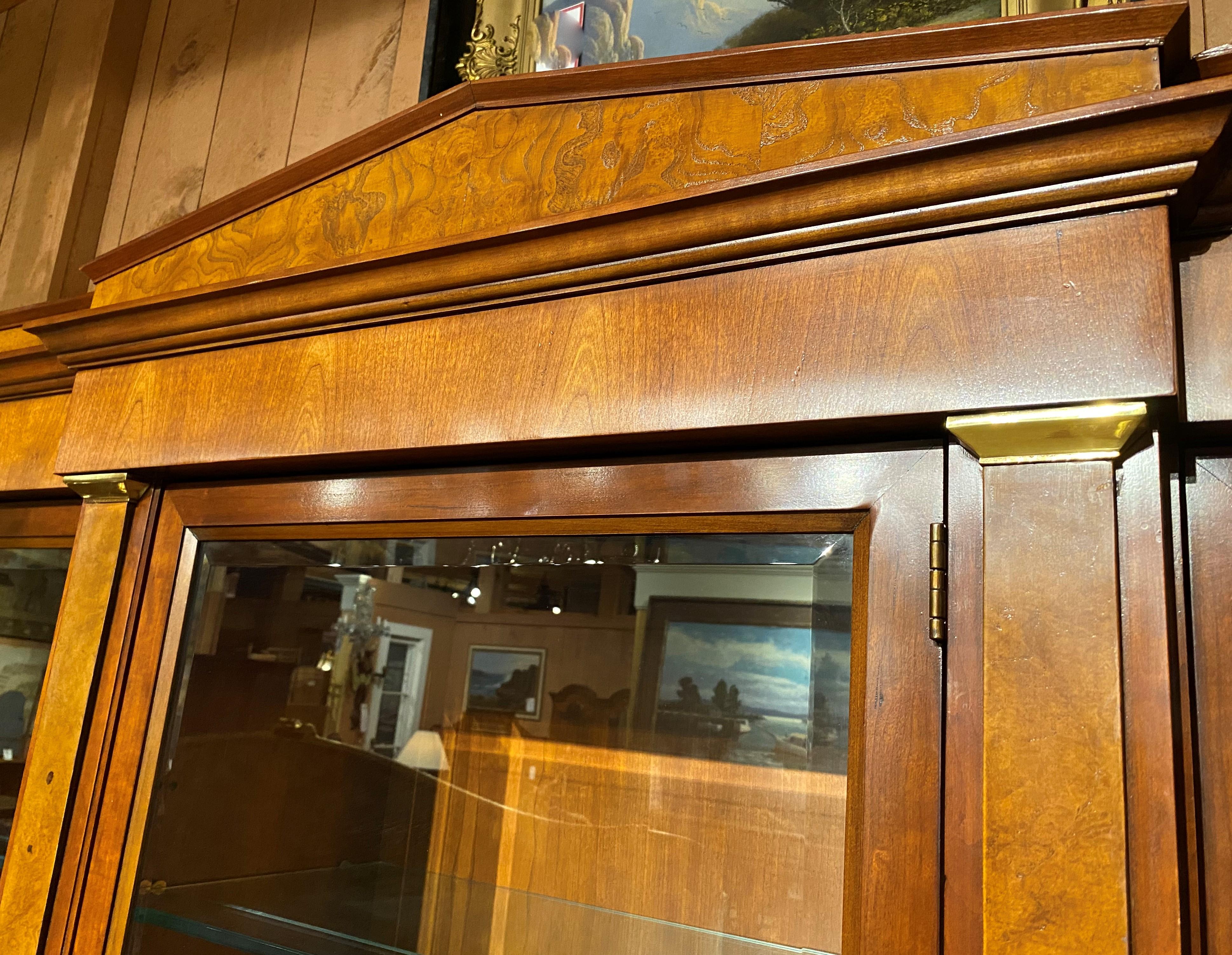 A Fine example of a two part fruitwood breakfront china cabinet, bookcase, or server, its upper case with a burled walnut veneer central pediment and molded cornice surmounting three beveled glass doors, opening to lighted glass shelf compartments,