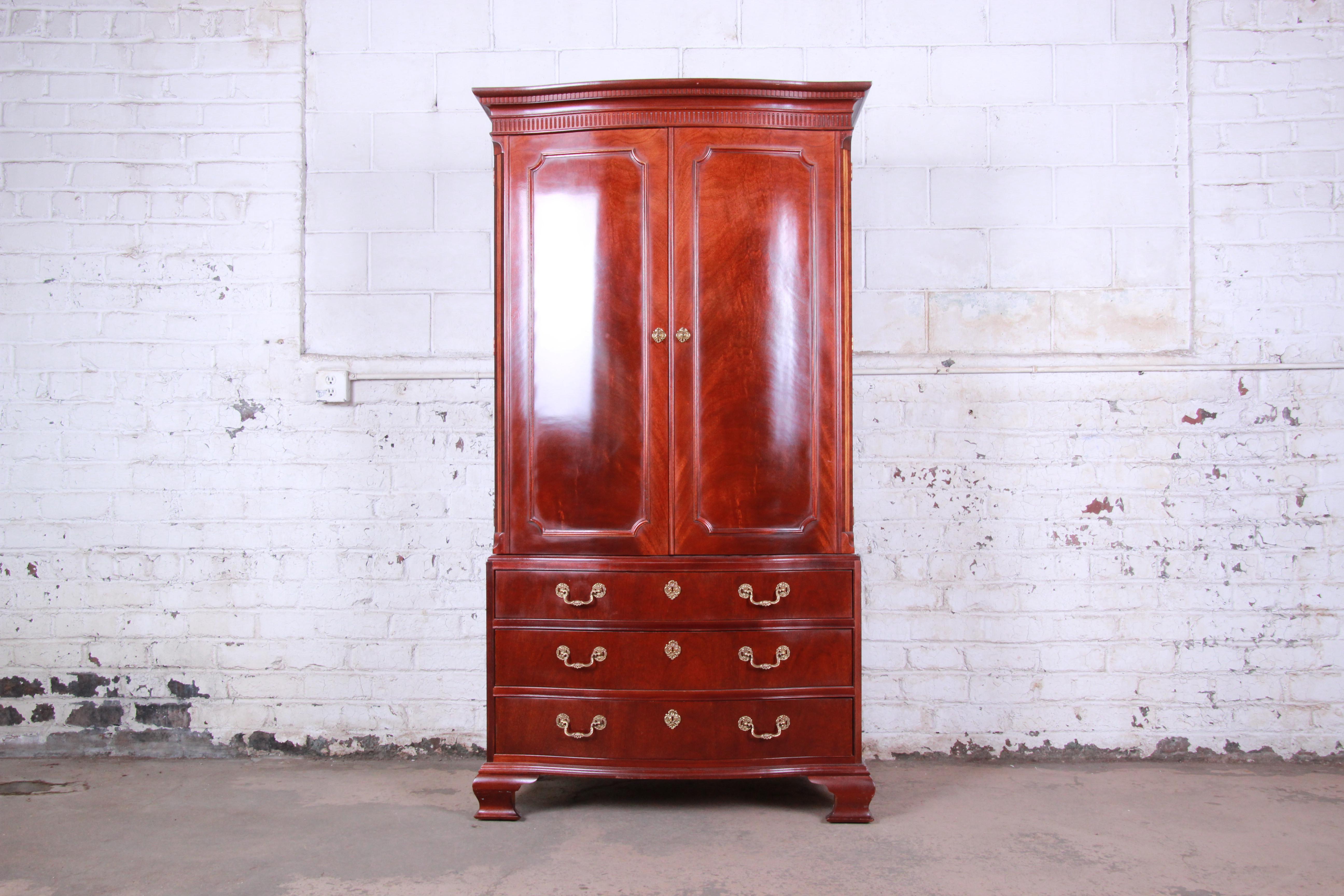 An exceptional Georgian style mahogany wardrobe or linen press by Baker Furniture. The chest features gorgeous mahogany wood grain with nice carved wood and inlaid details. It offers excellent storage, with three cubbies and two adjustable shelves