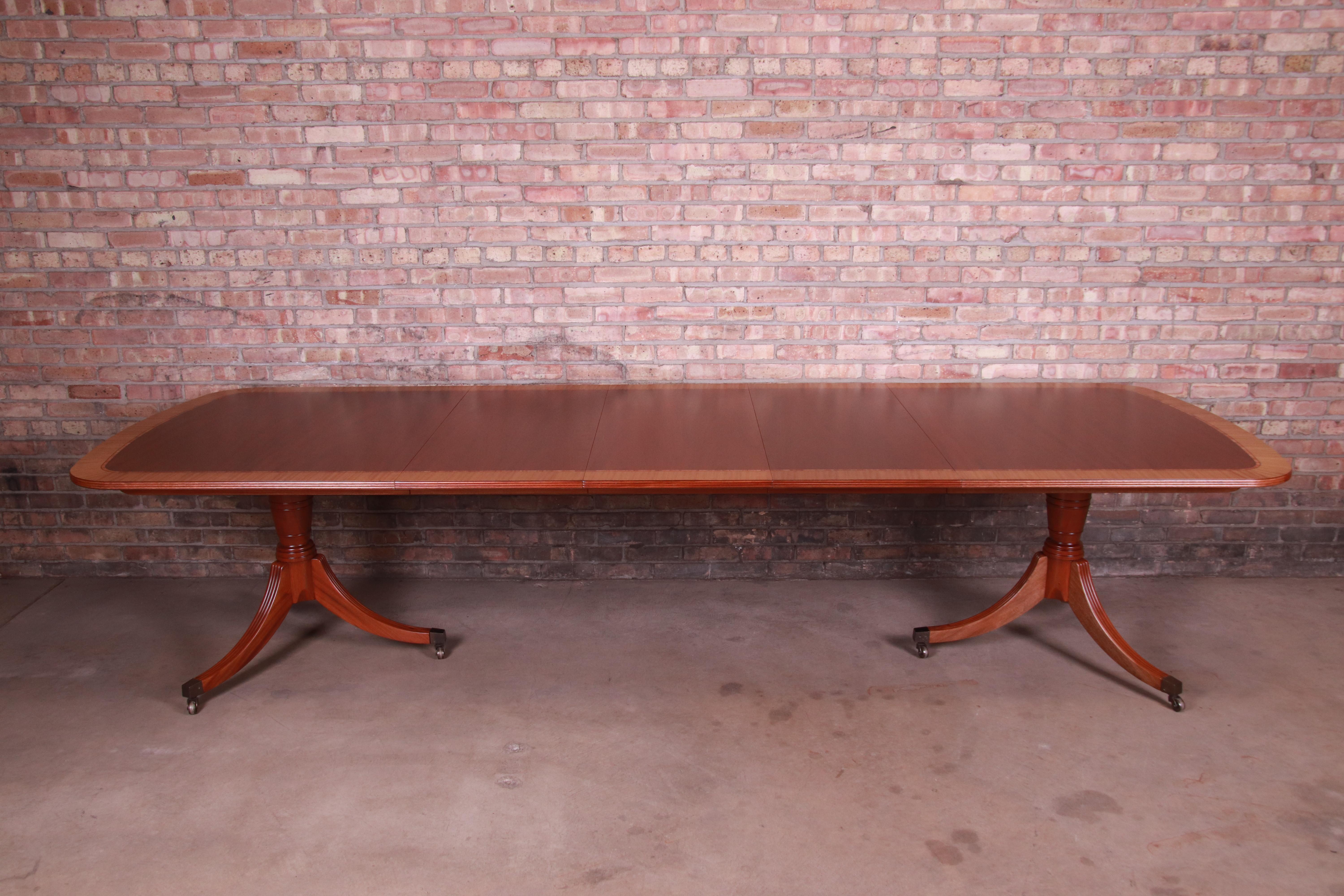 An exceptional Georgian style extension double pedestal dining table.

By Baker Furniture

USA, late 20th century

Book-matched mahogany with satinwood banding, carved solid mahogany pedestals, and brass-capped feet.

Measures: 76